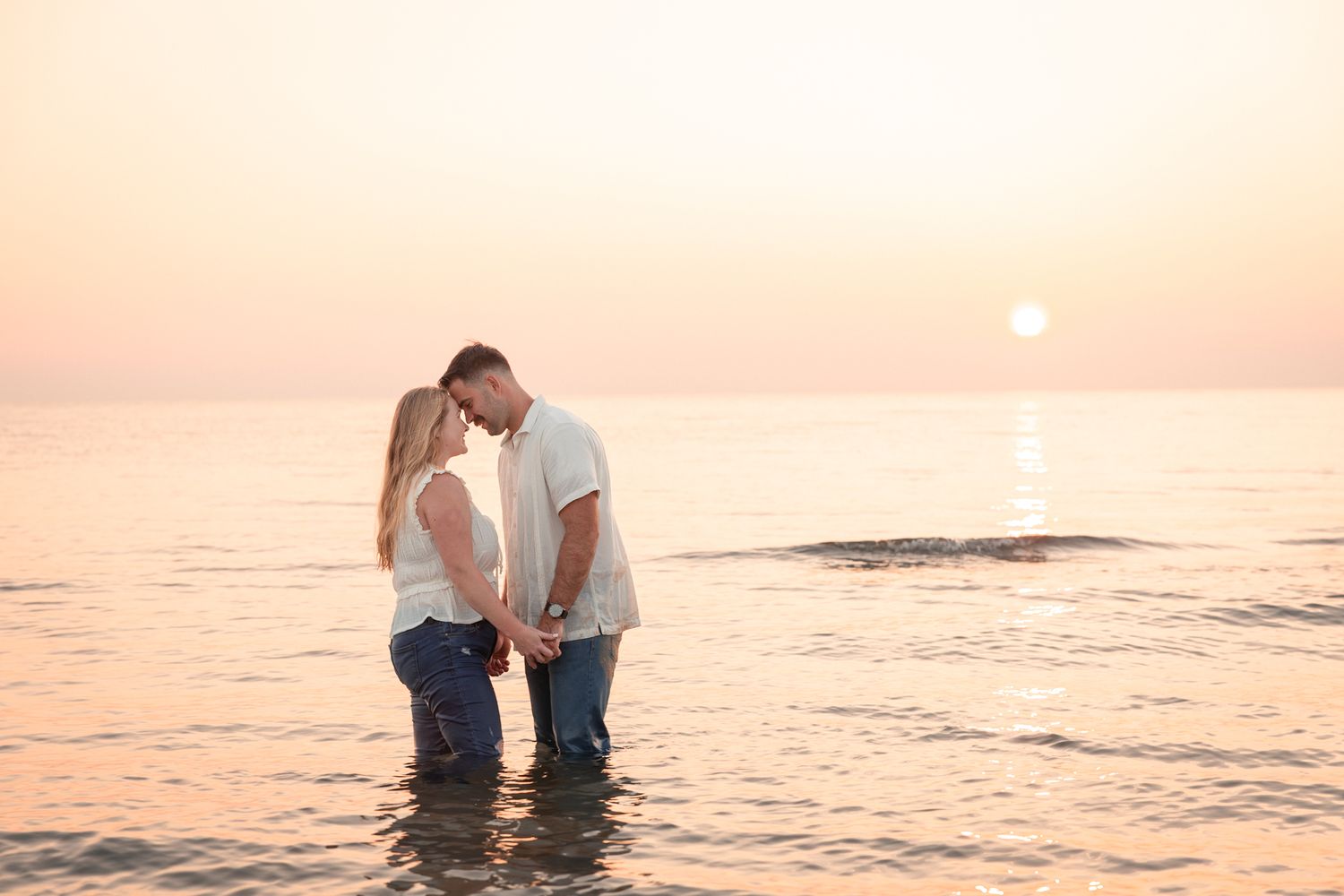 Intimate couple embracing in shallow ocean water at sunset.