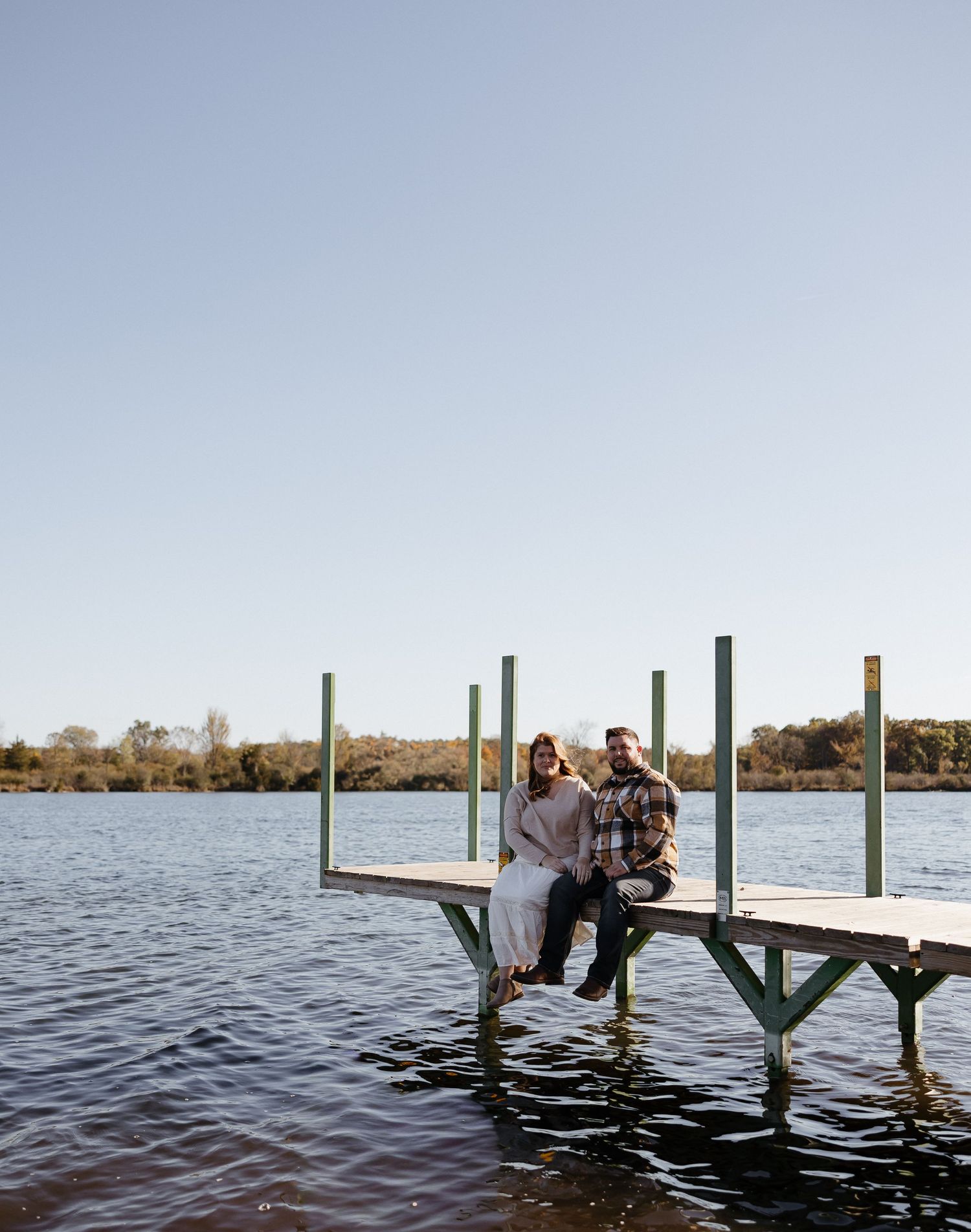 Couple sits romantically on wooden dock overlooking serene lake waters.