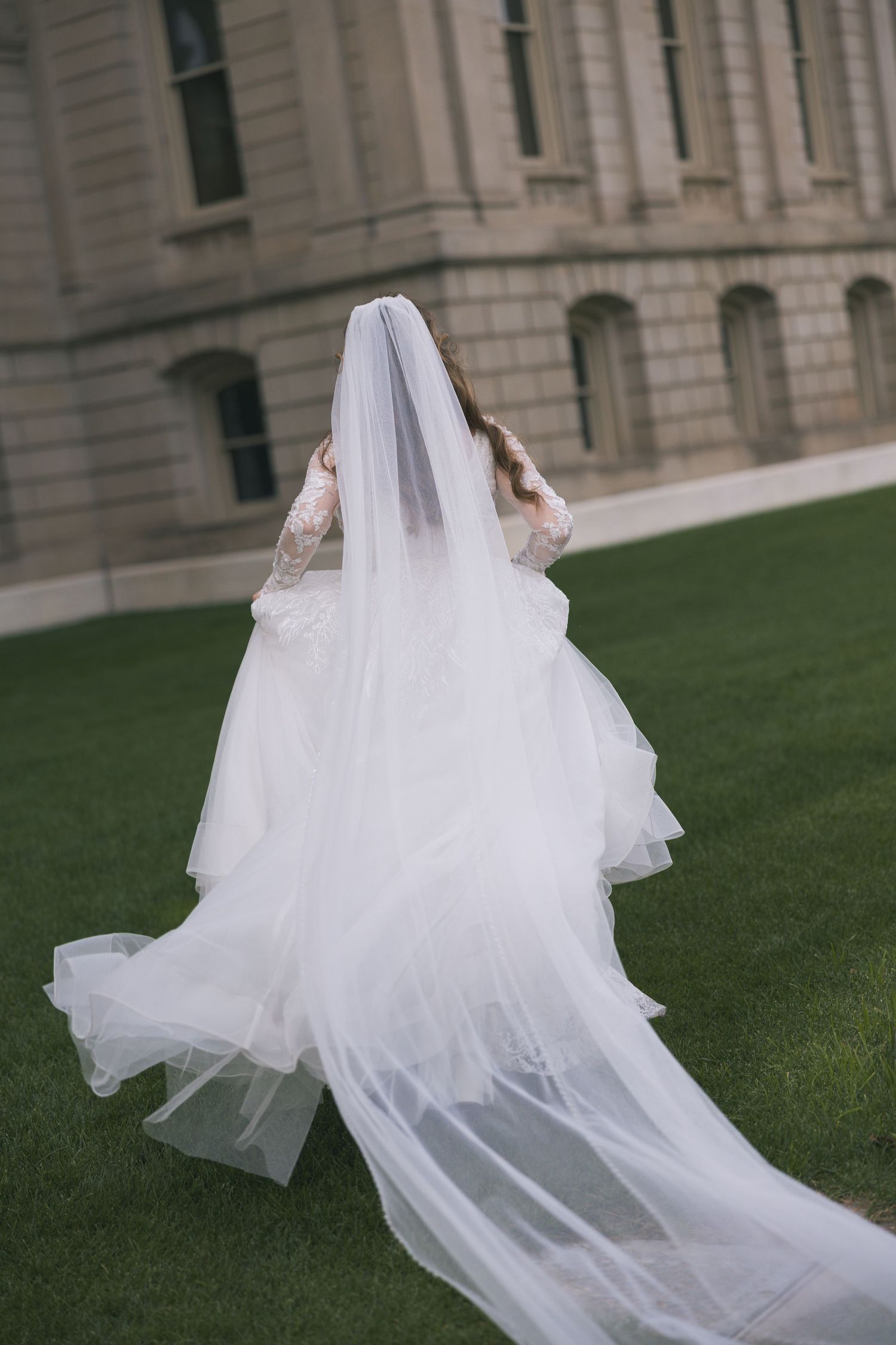 Flowing white wedding dress train spreads across green lawn in artistic shots.