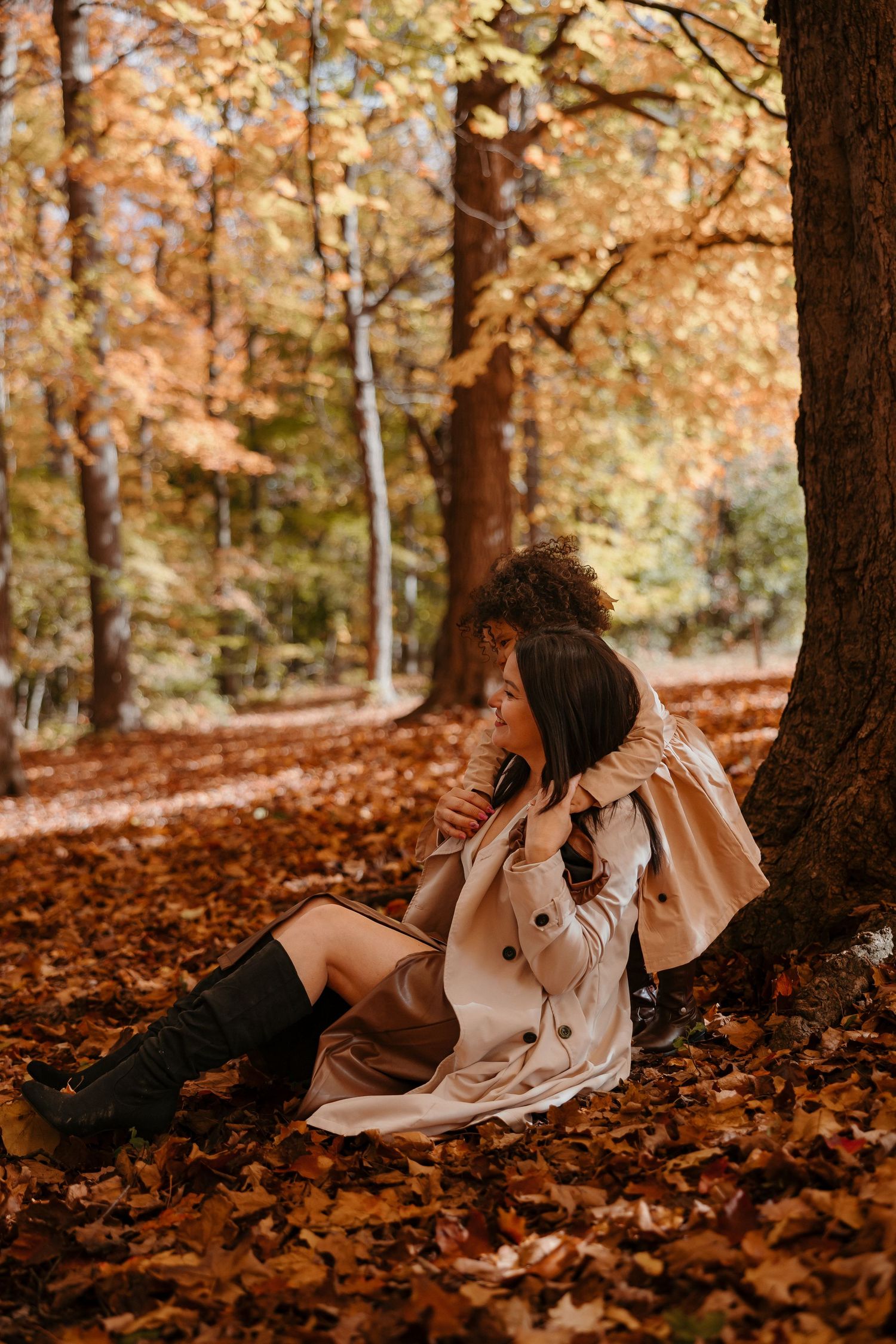 A person in a flowy beige dress lies on autumn leaves beneath a tree in a dreamy forest setting.