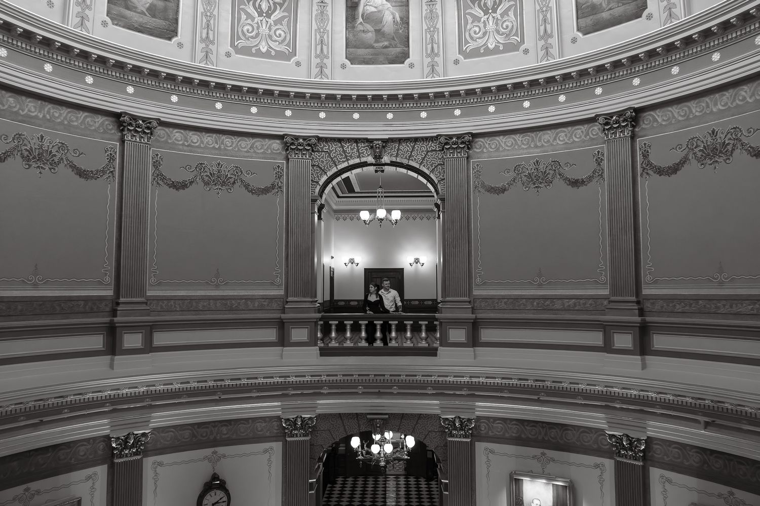 Black and white photo of an ornate rotunda interior with balcony, columns, and chandelier in a historic government building.