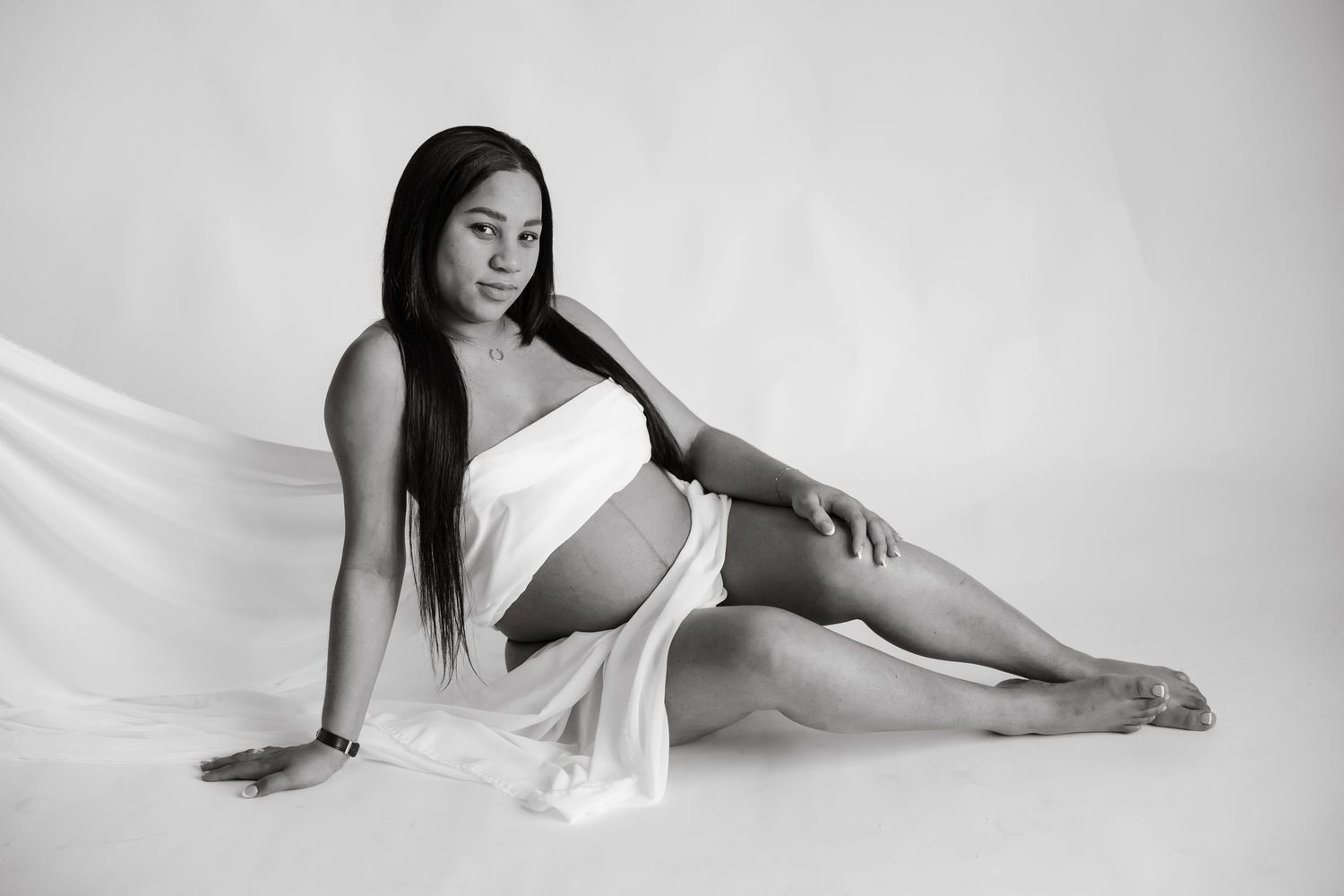 Artistic black and white maternity photos showing a woman in white fabric against light background.