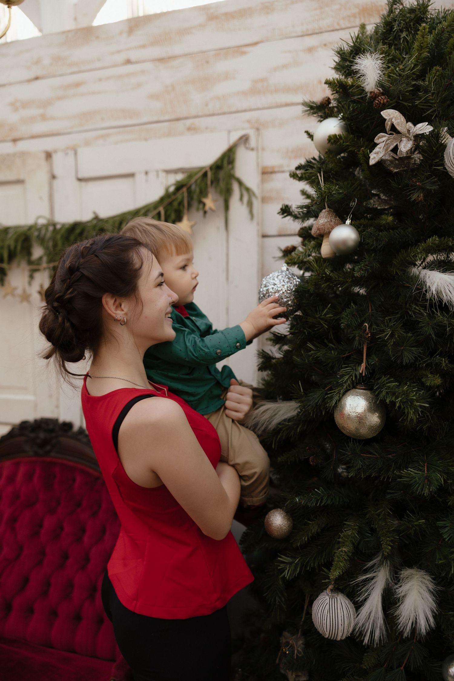 A child in red decorates a Christmas tree with silver ornaments.