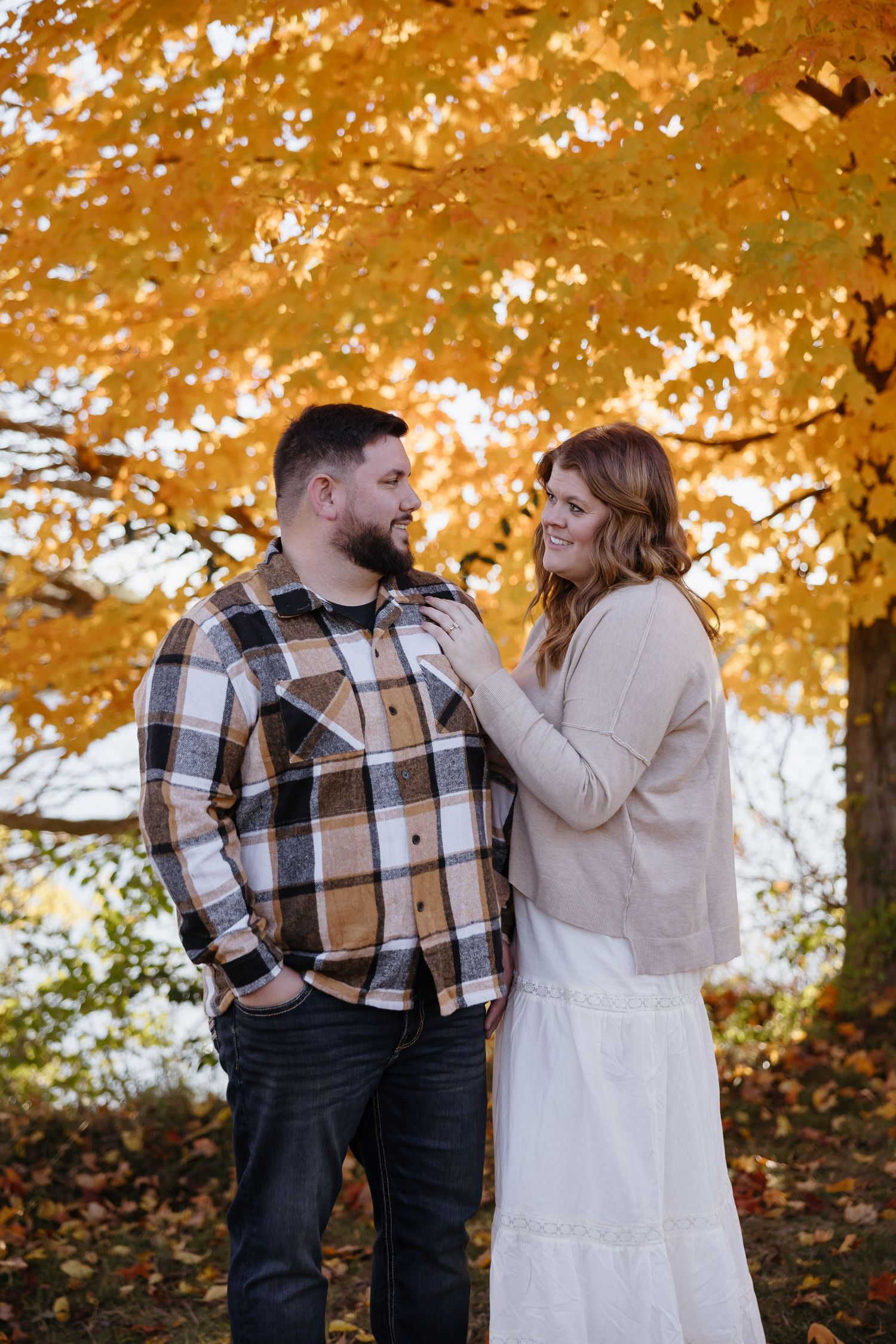Couple shares joyful moment against vibrant orange autumn trees.