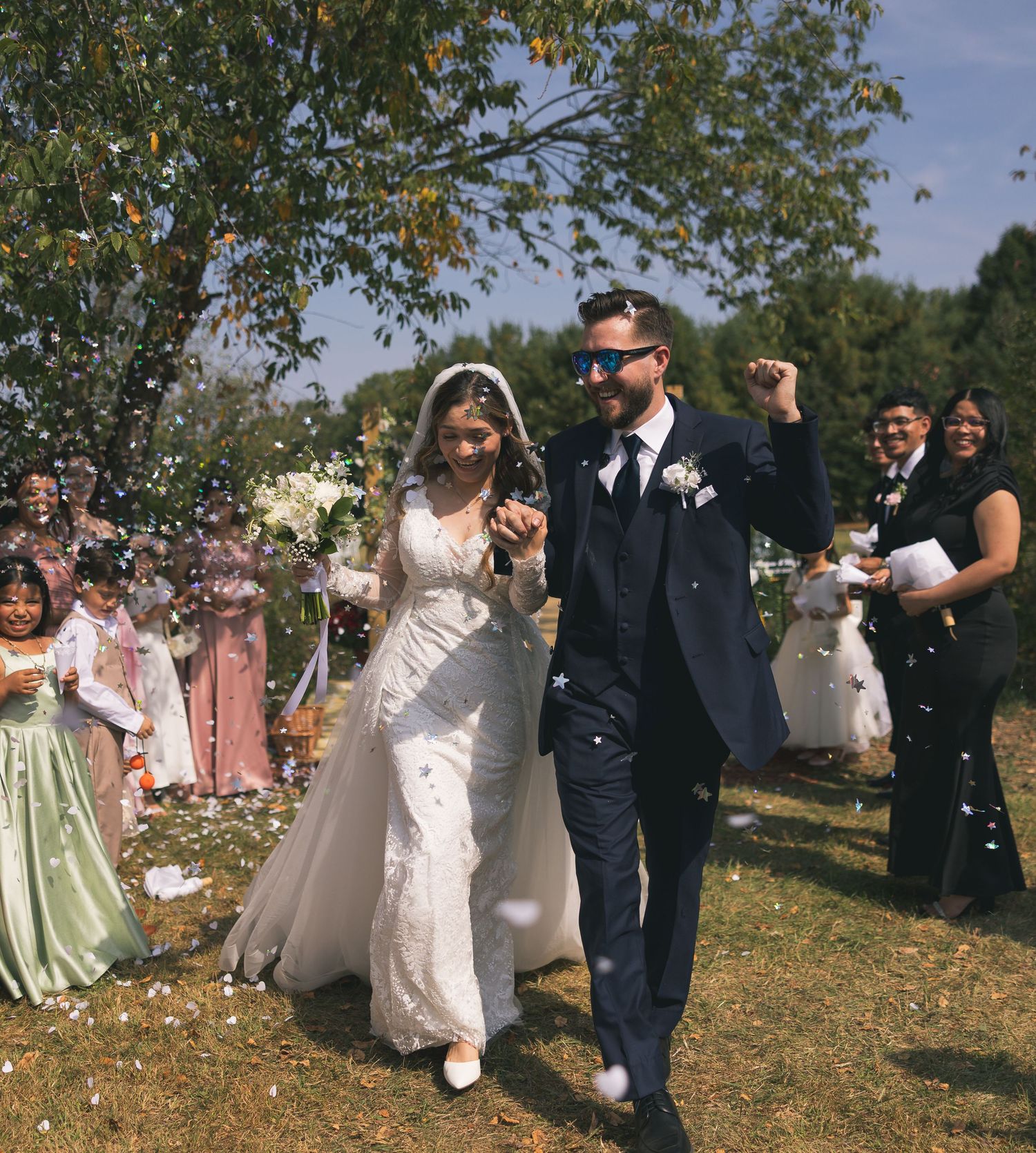 Wedding party celebrates outdoors throwing flower petals in a joyful scene.