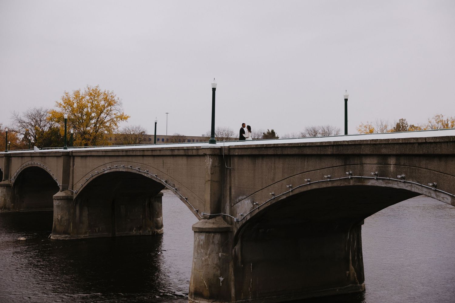 Panoramic view of a stone bridge over calm water during autumn.