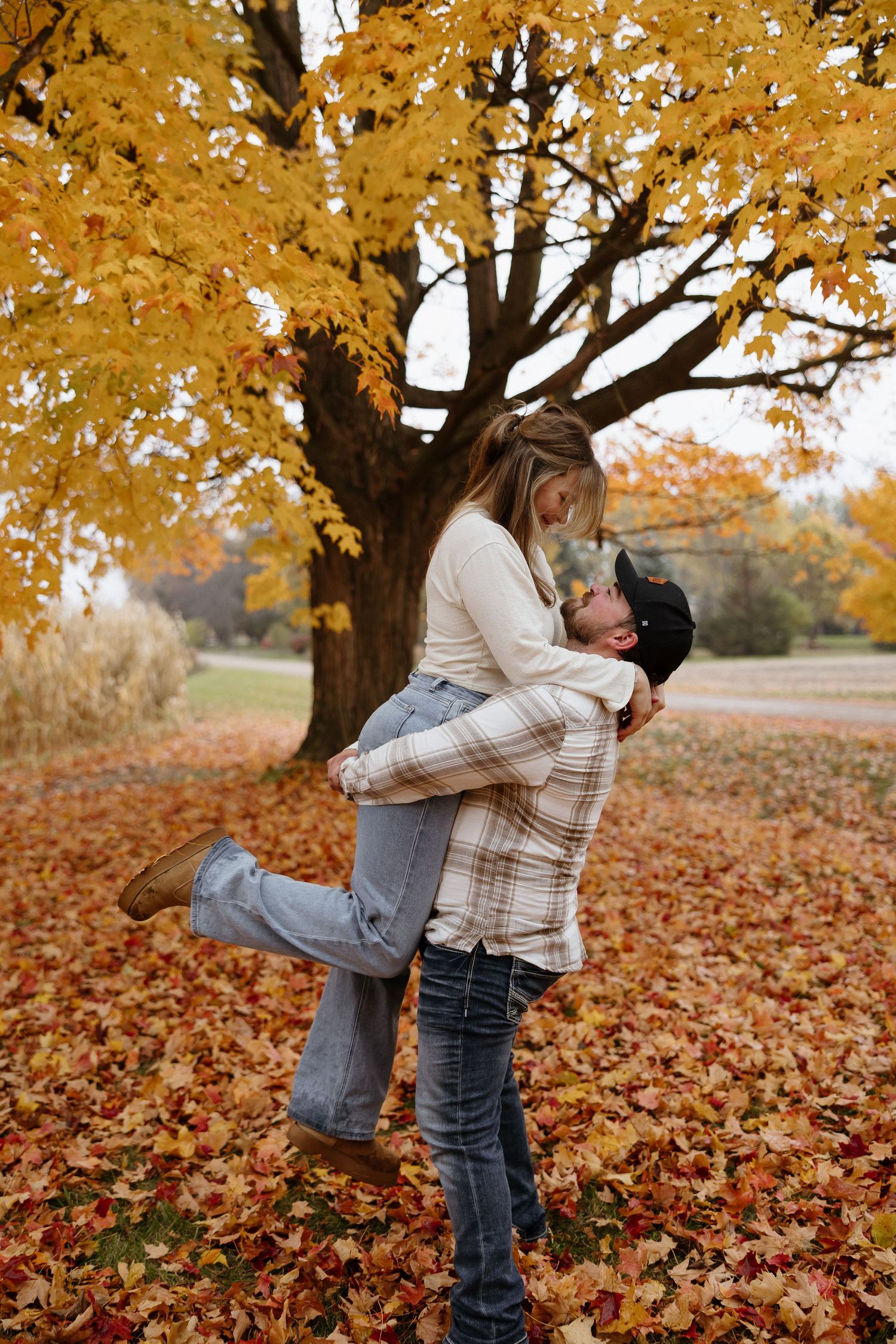 A romantic fall engagement photo with a couple embracing under golden autumn trees.