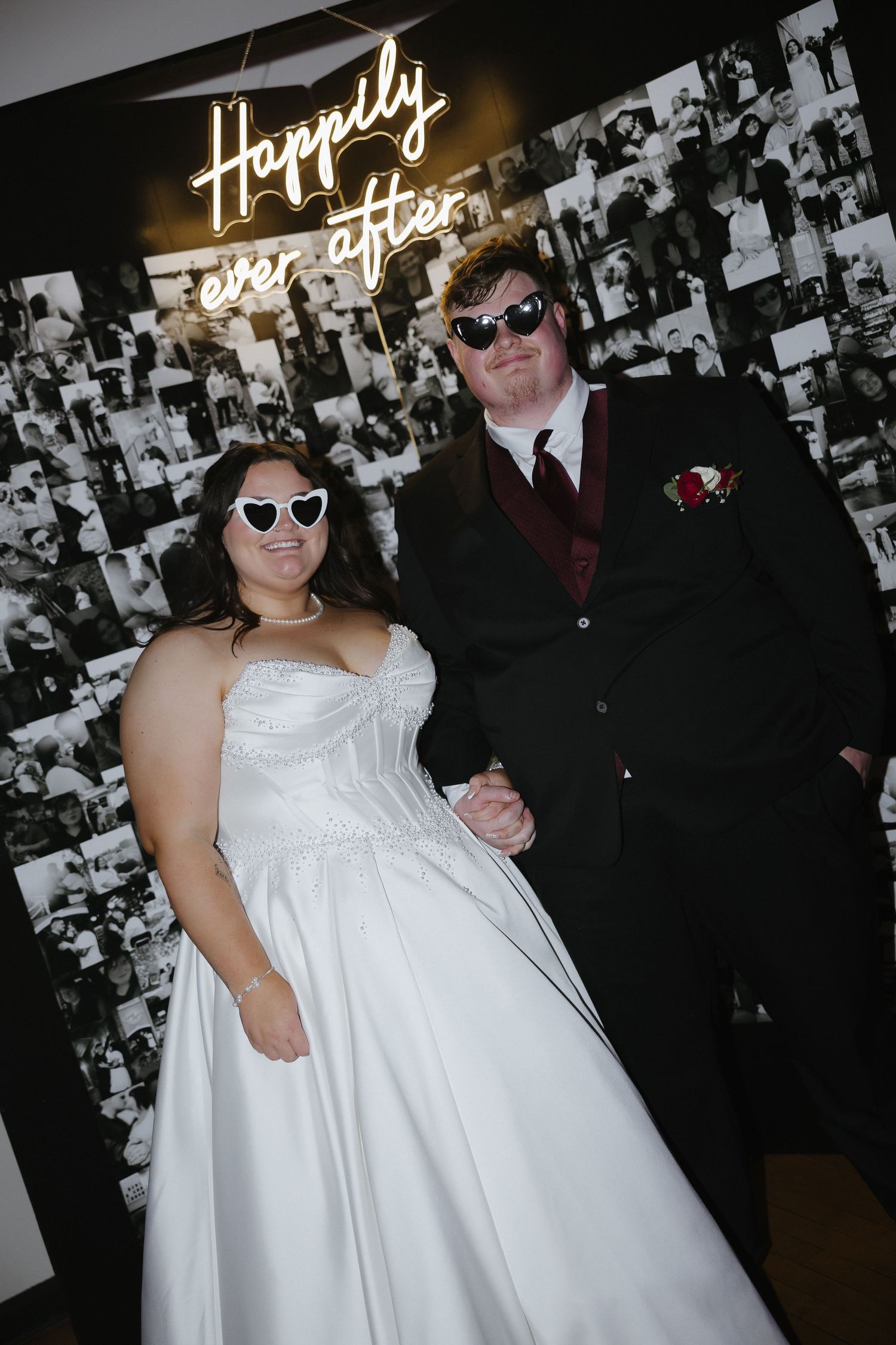 Bride and groom wearing fun sunglasses pose in front of a Happily Ever After neon sign at their wedding reception.