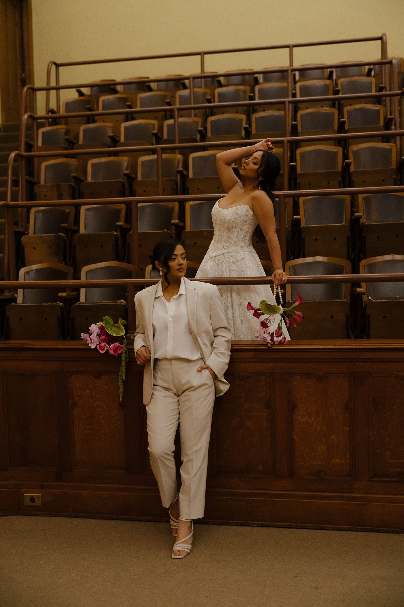 A figure in all-white attire poses gracefully against wooden stadium seating in a performance space.