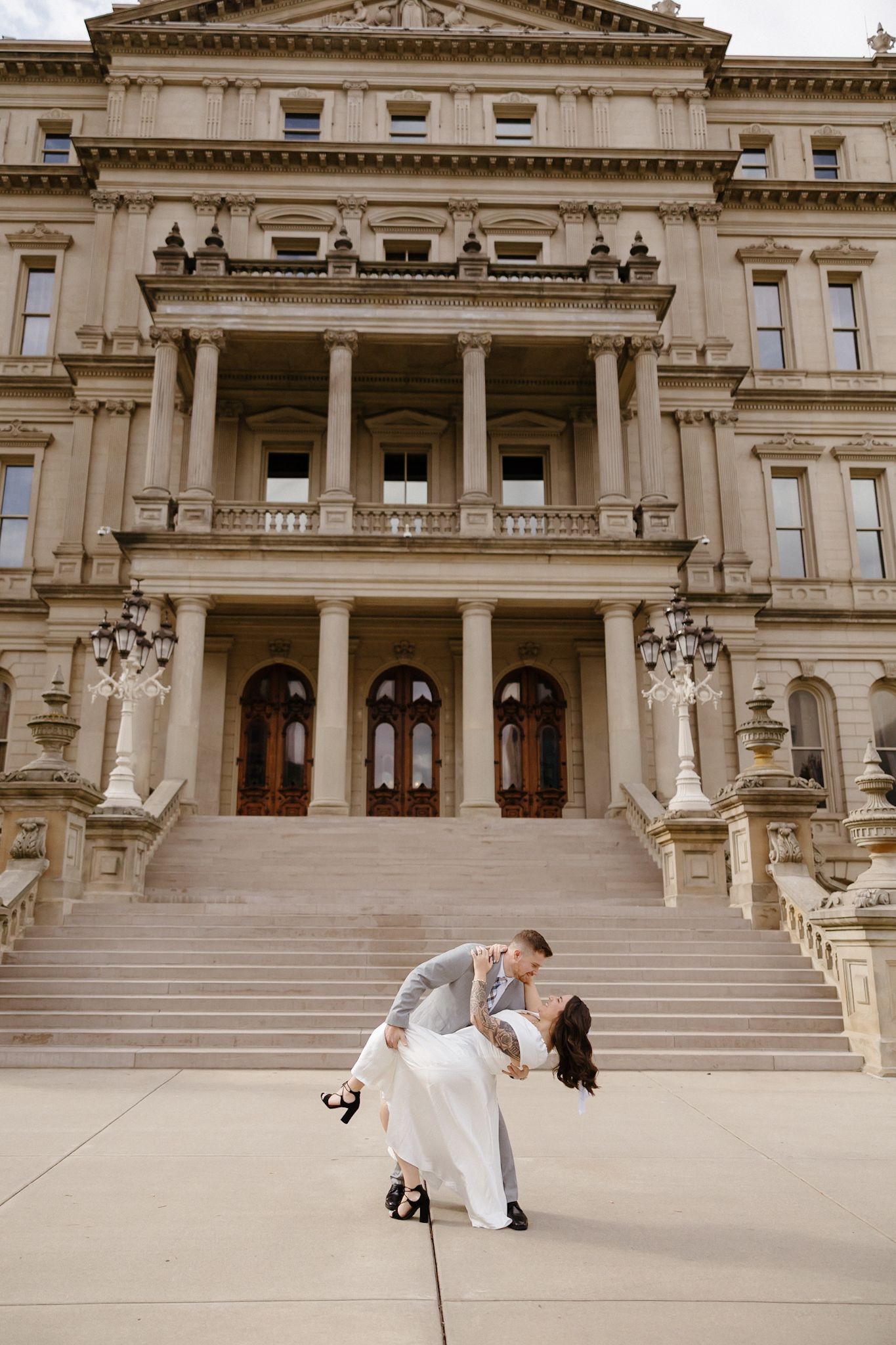 Wedding couple performs playful dance moves on ornate stone courthouse steps.