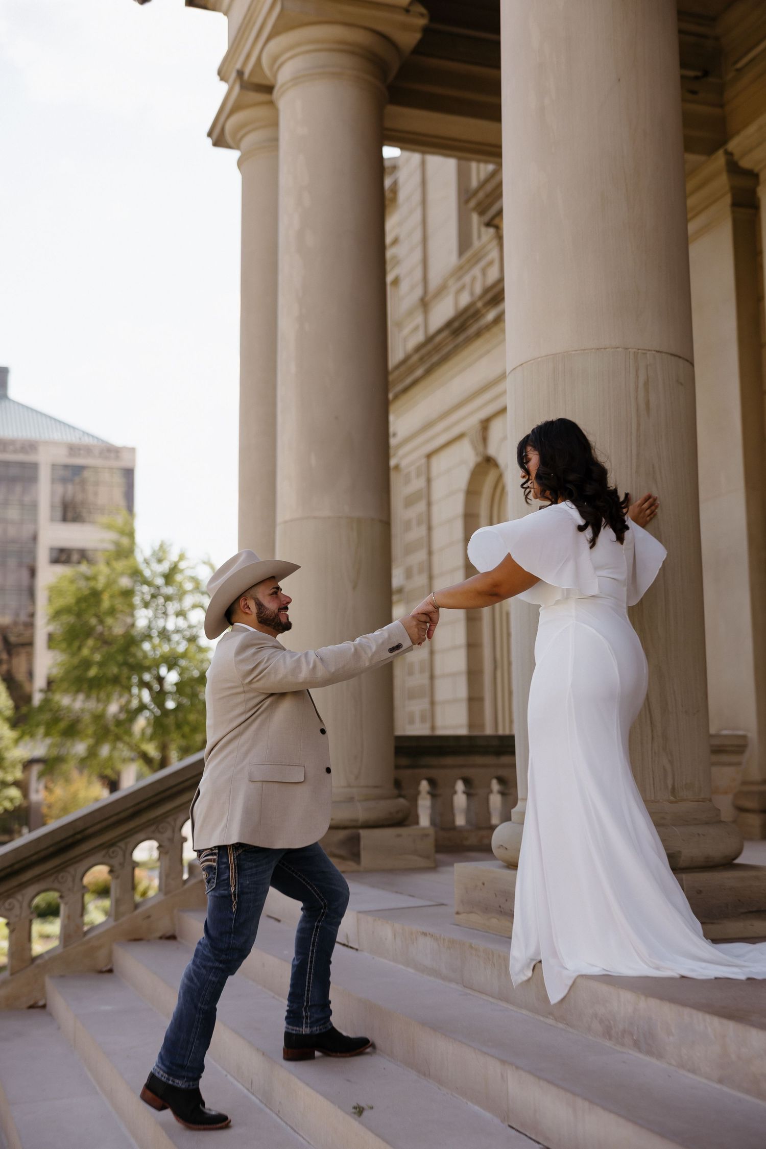 Playful couple in white clothing dances under classical stone colonnade.