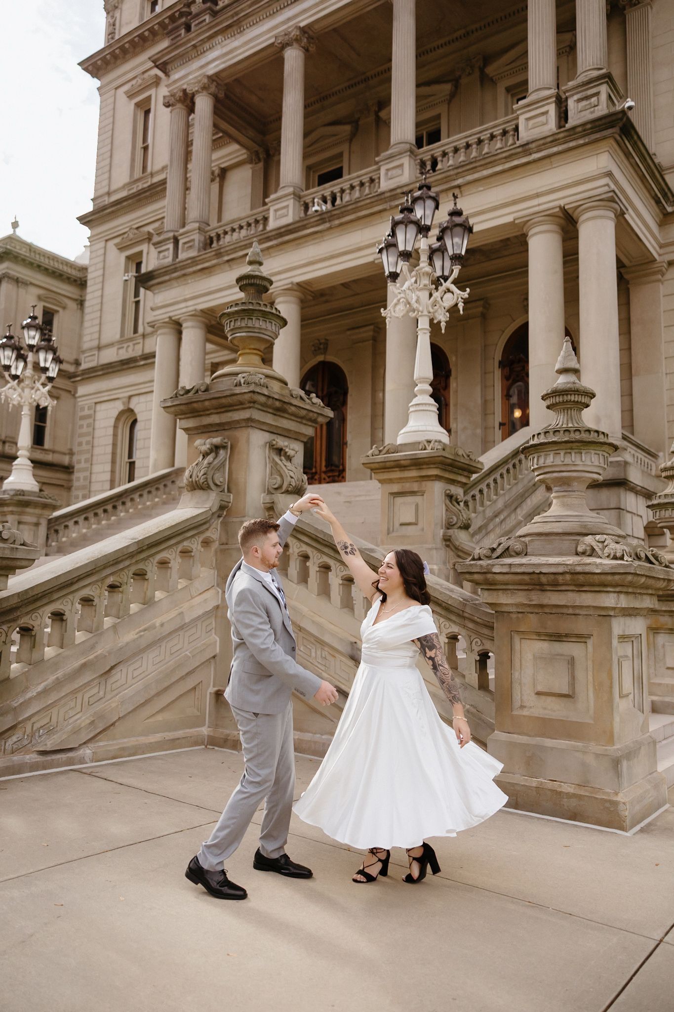 A couple in wedding attire dances elegantly on grand marble steps of a historic building.