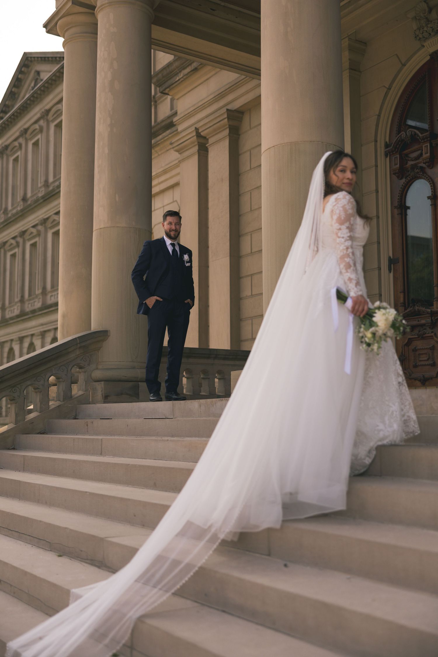 Elegant wedding photos on grand stone steps showcase bride's flowing veil and gown.
