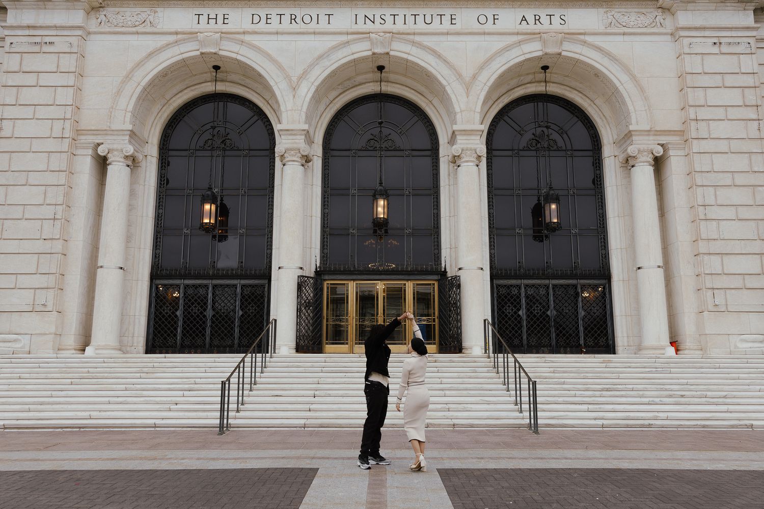 Couple sharing a romantic kiss on the steps of the Detroit Institute of Arts museum entrance.