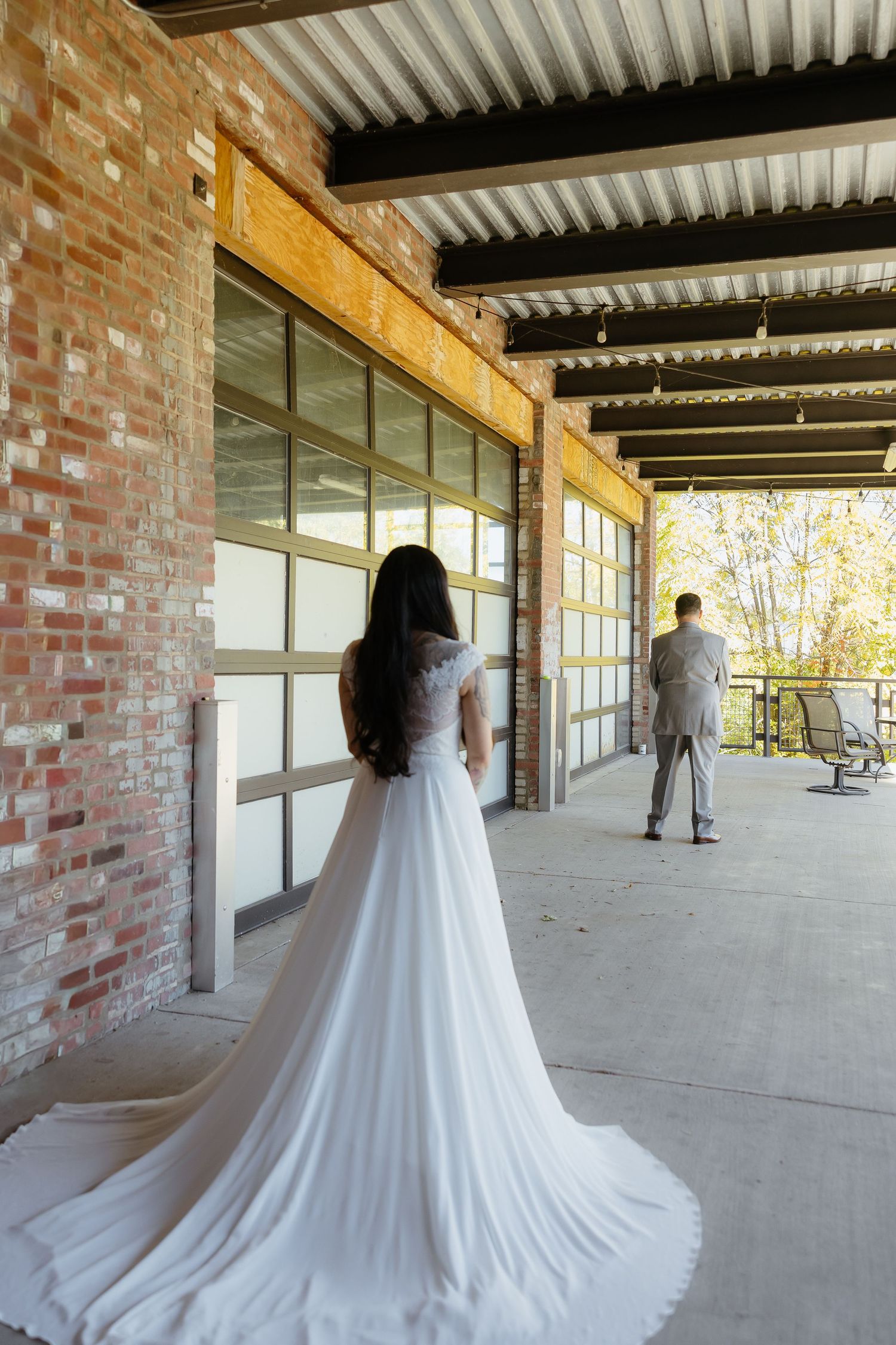 Bride in white gown with long train approaches groom in suit during wedding first look at brick venue.