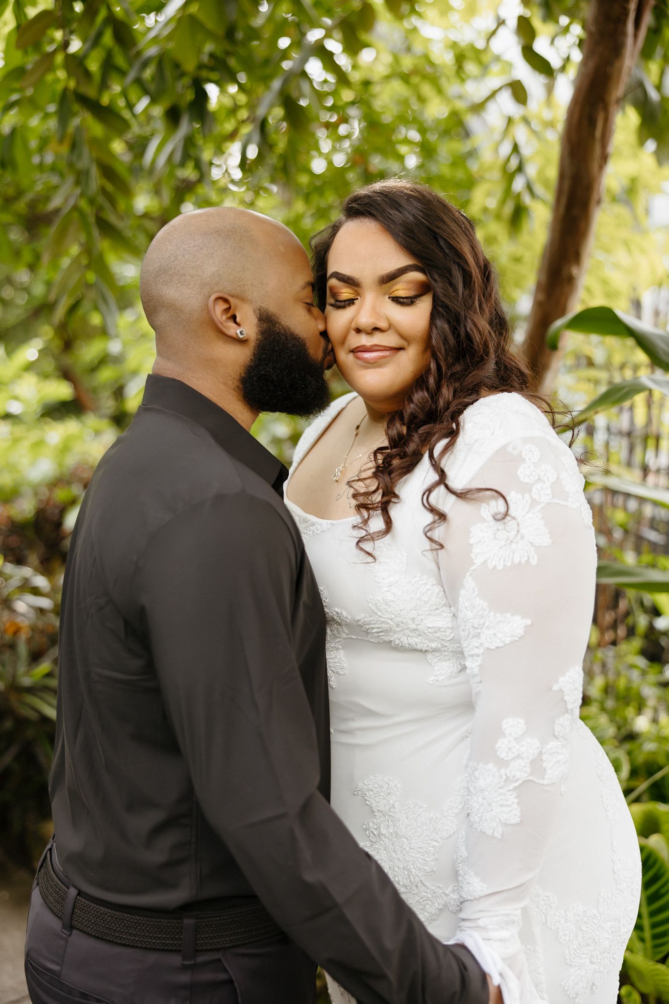 A couple shares an intimate moment in a garden setting wearing black and white formal attire.