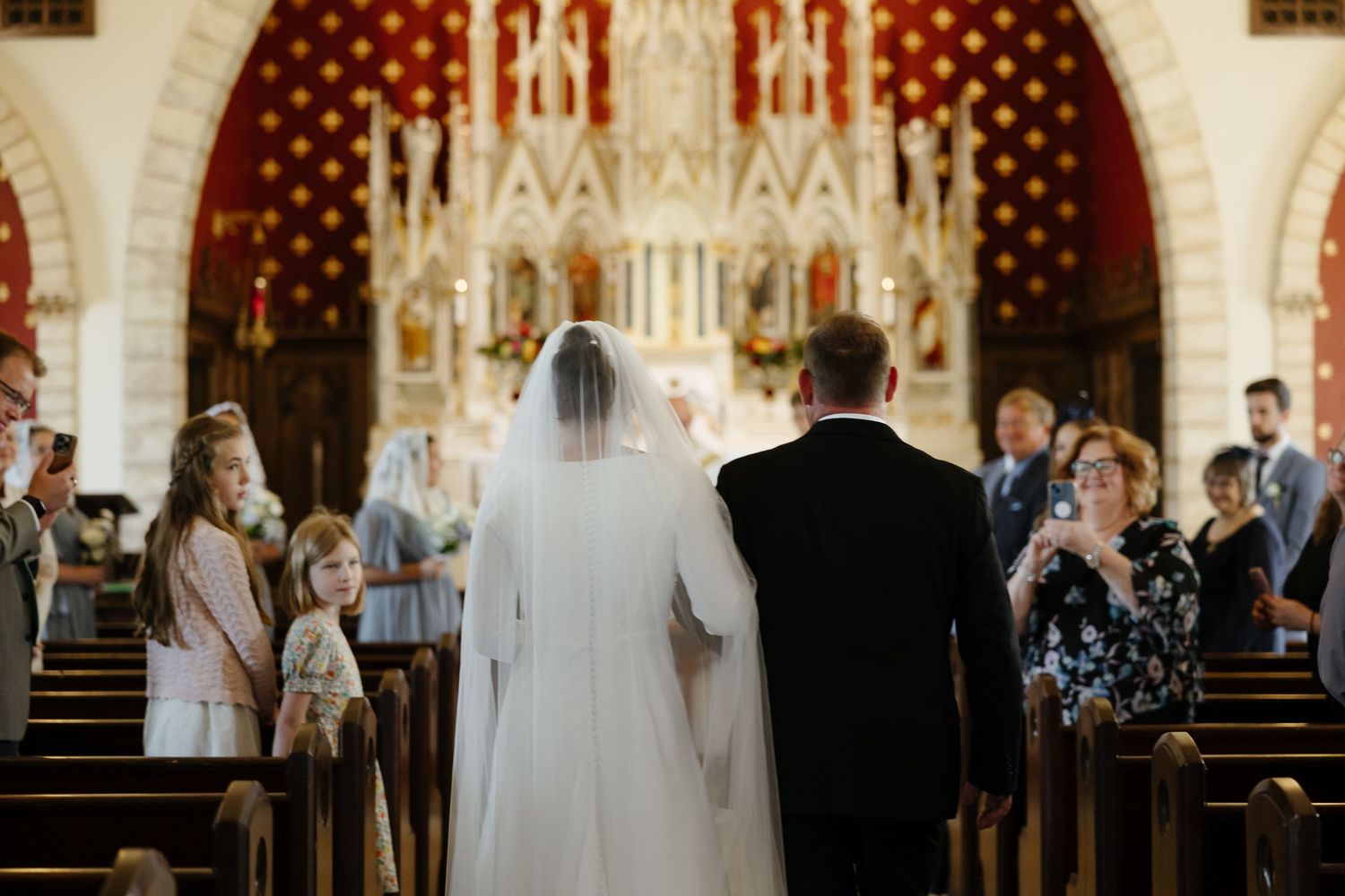 Wedding ceremony inside an ornate gothic church with decorative red and gold walls.