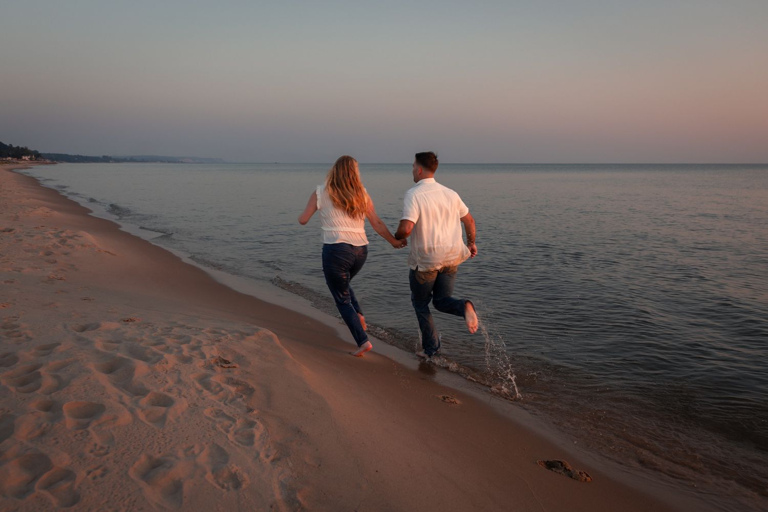 Couple walking together on a sandy beach at sunset.