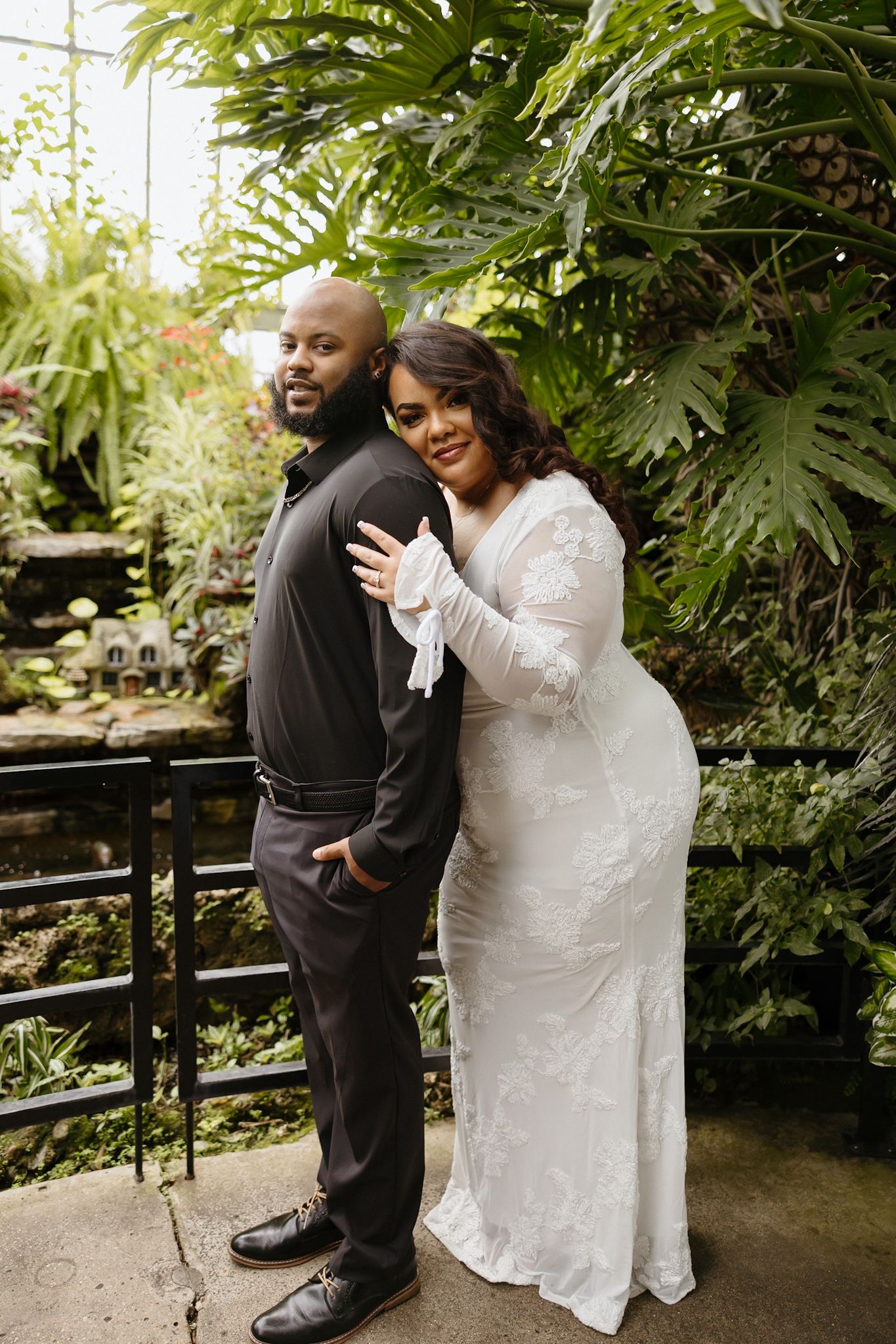 A couple shares joyful moments together on a garden bench surrounded by greenery.
