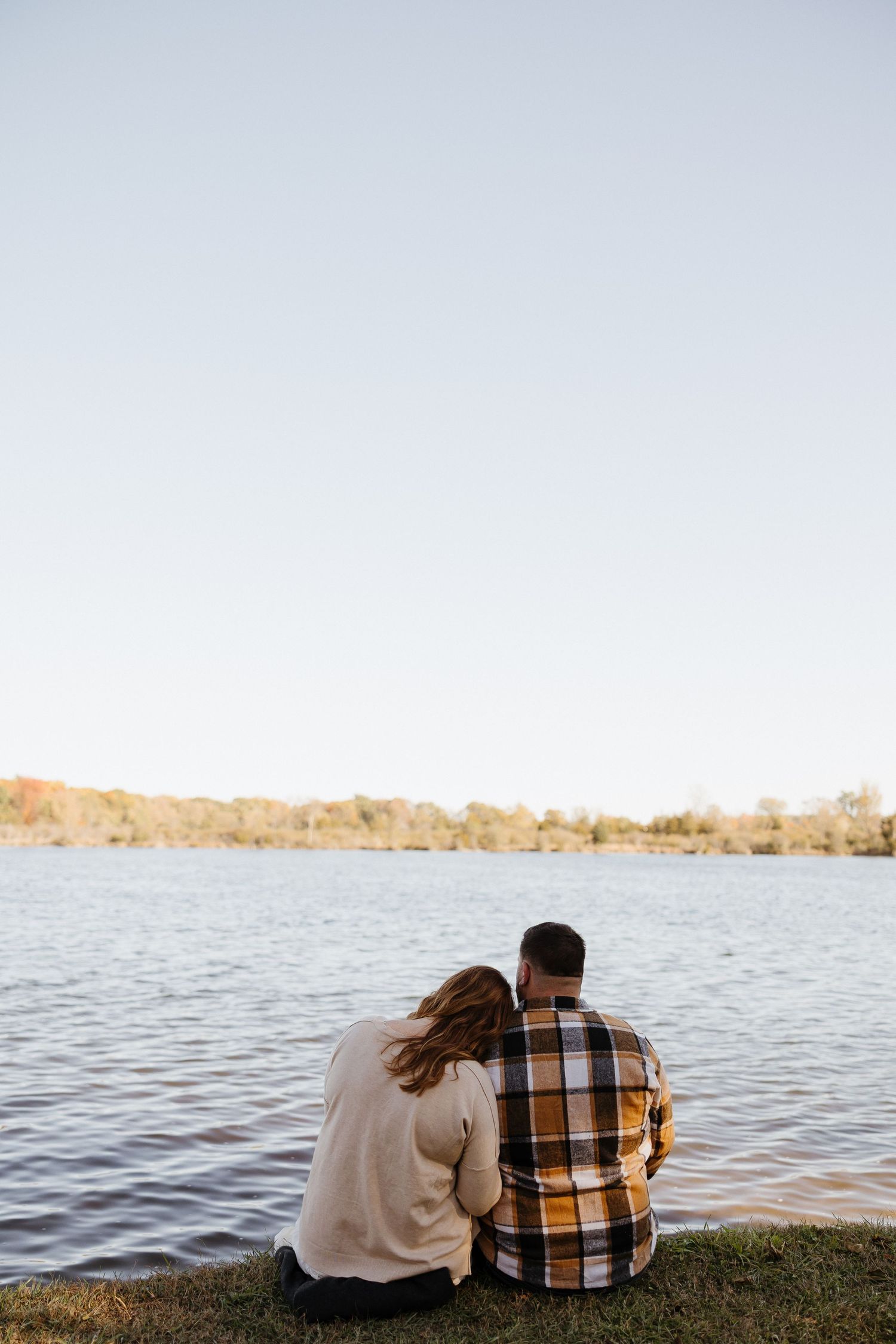 Couple sits together by a serene lake at sunset sharing an intimate moment.