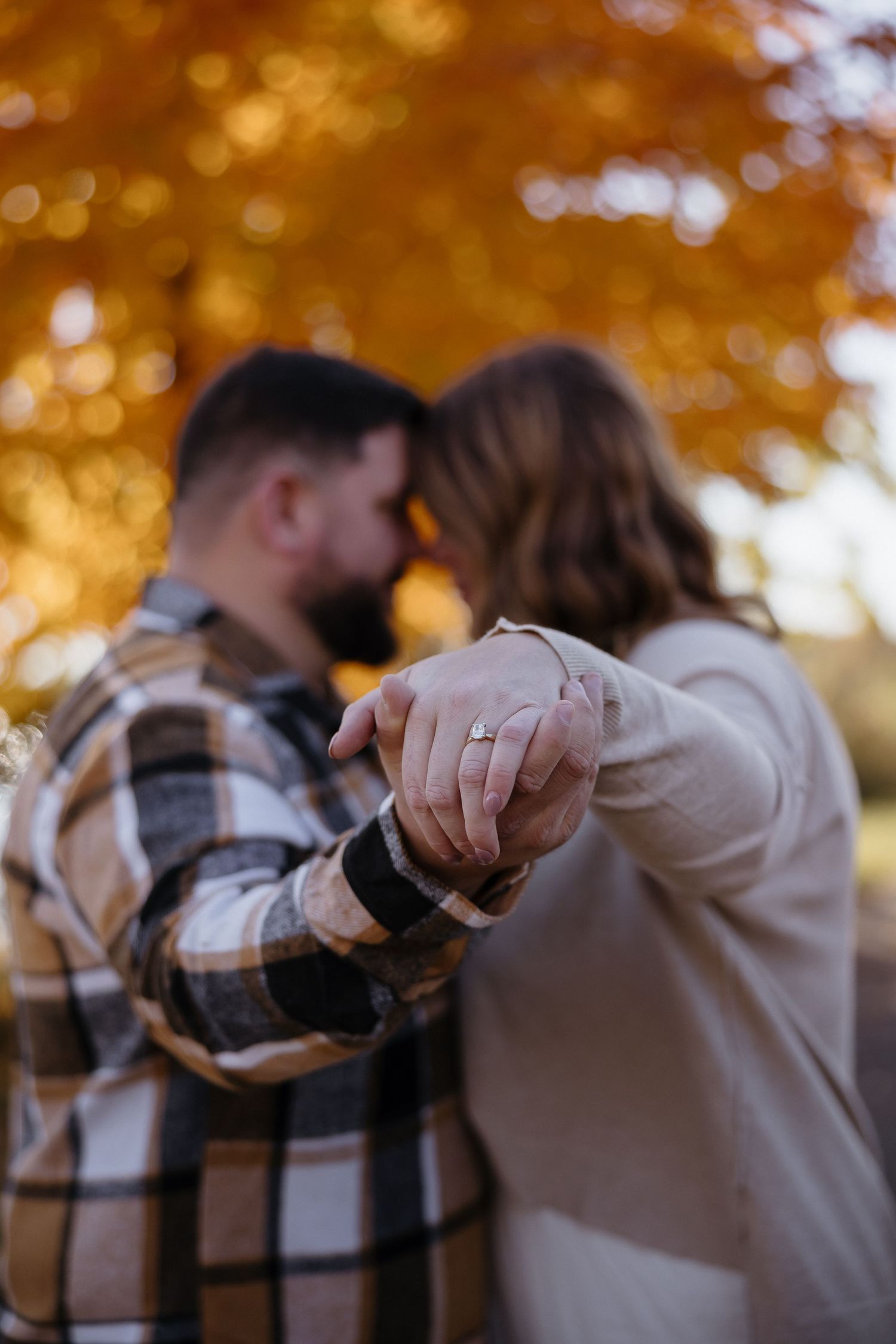 Autumn engagement photoshoot with golden bokeh and fall foliage in background.