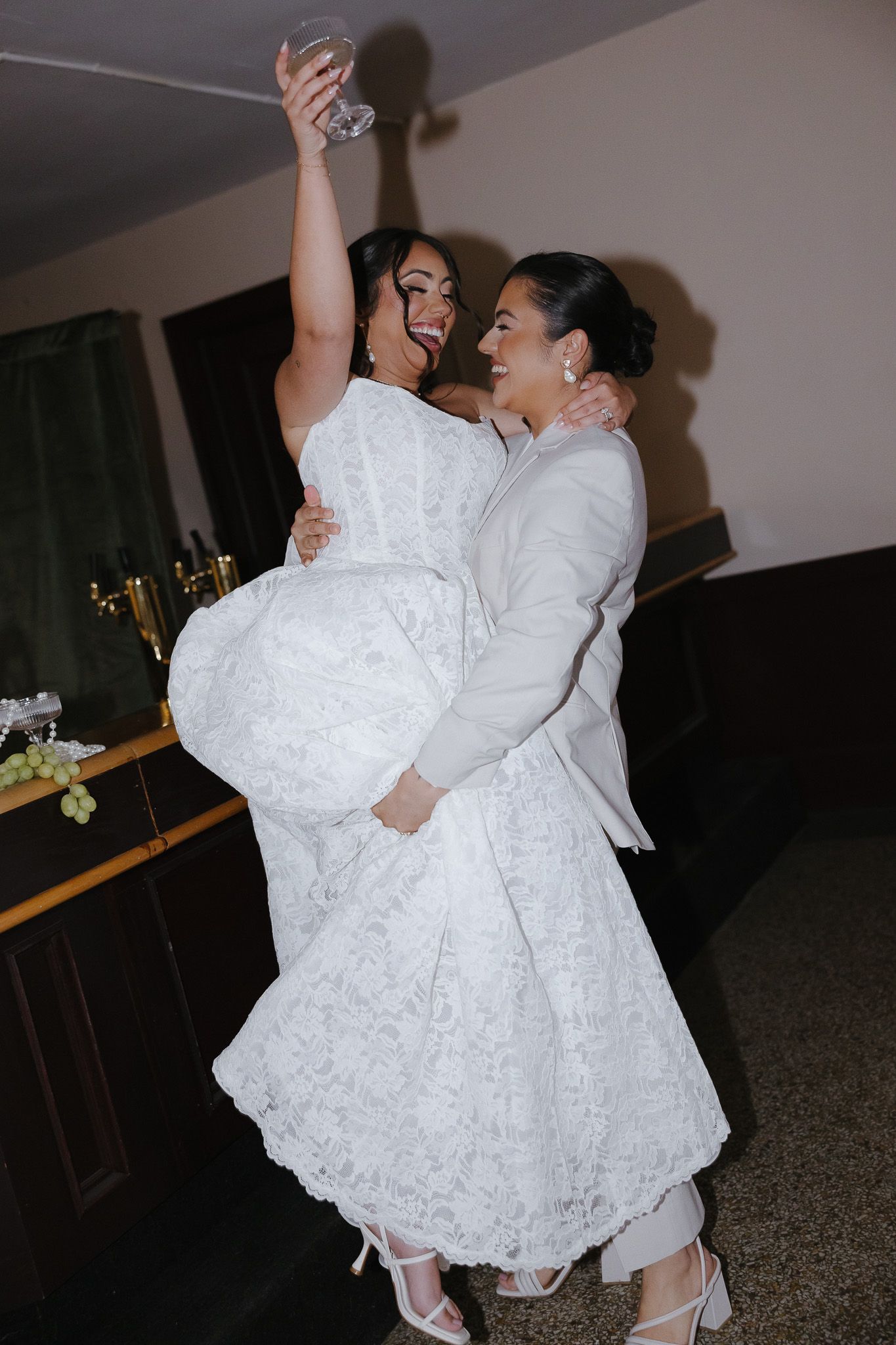 Newlyweds dance together in a dimly lit room wearing white formal attire.