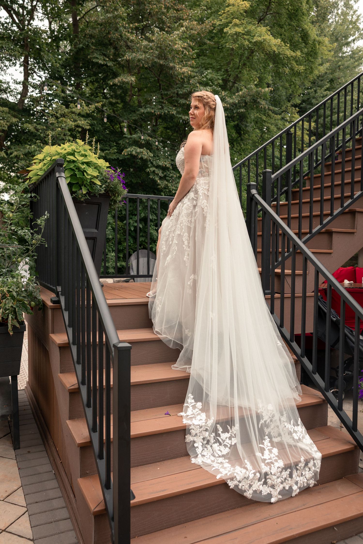 An elegant lace wedding dress with flowing veil photographed on wooden deck stairs.