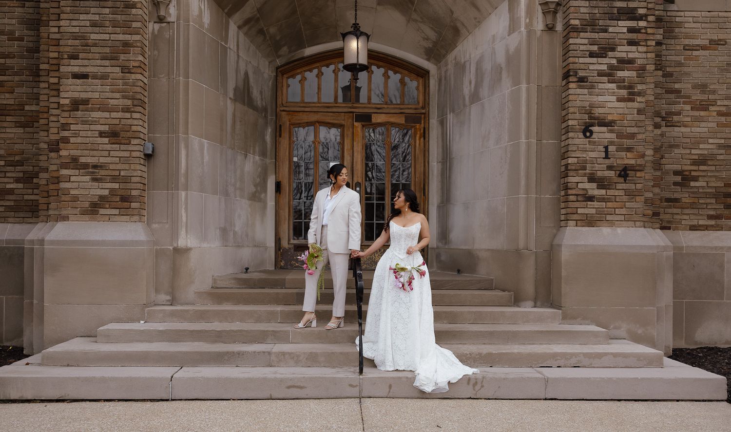 A couple in wedding attire stands on stone steps in front of an ornate wooden church entrance.