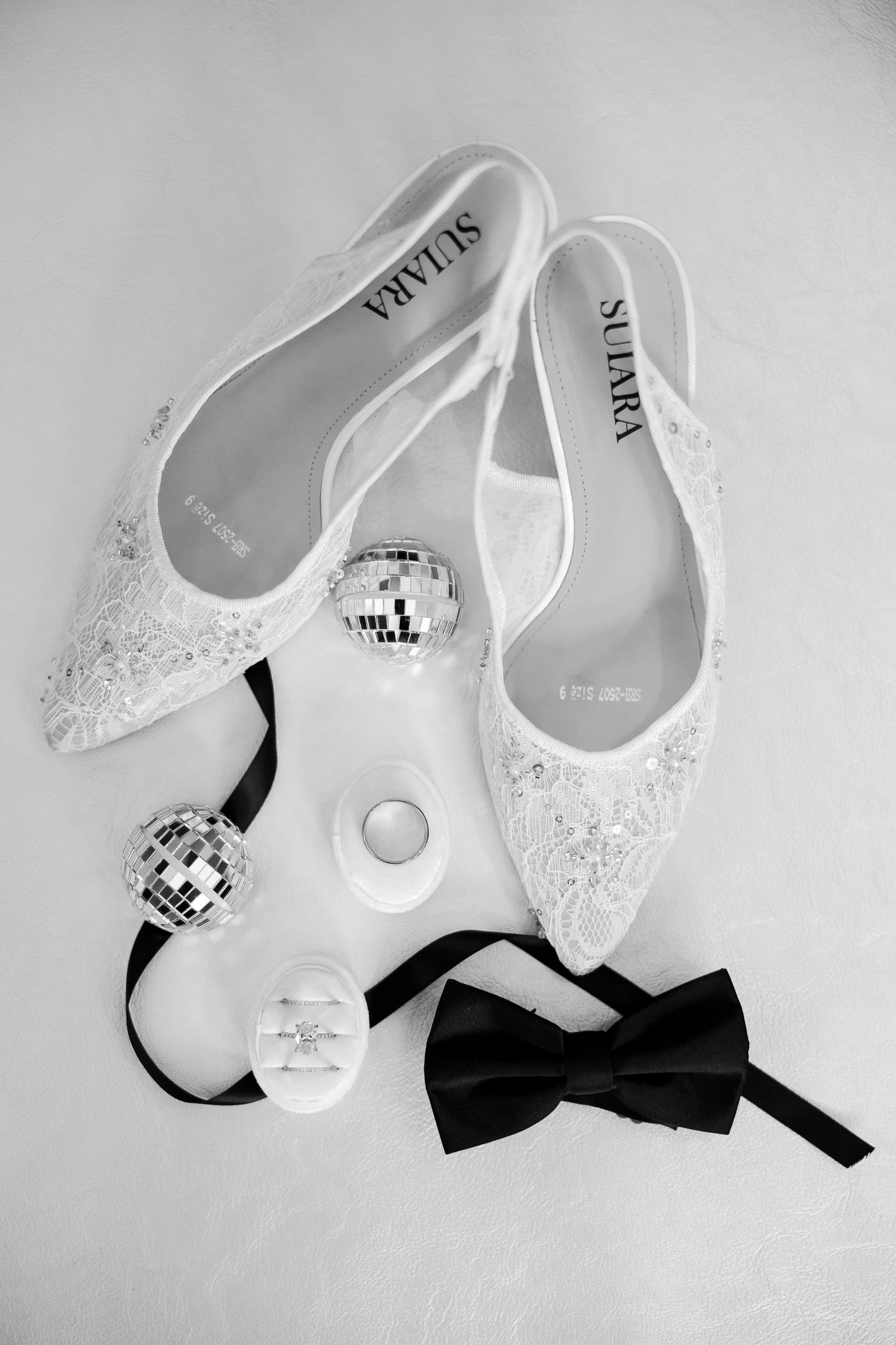 Black and white flat wedding shoes by Sulara with bow tie, rings, and disco balls bridal accessories.