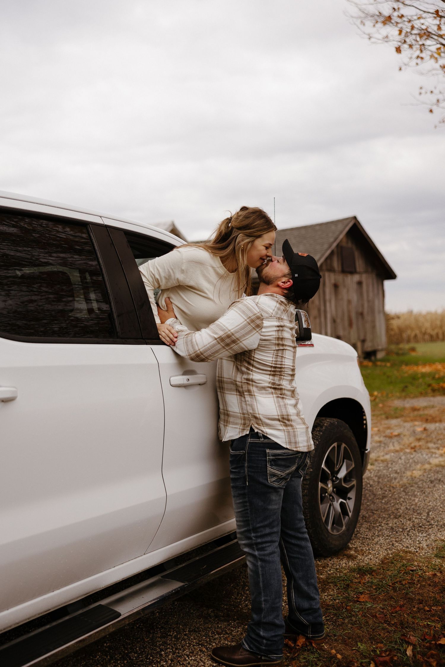 A romantic moment captured beside a white SUV with a rustic barn in the background.