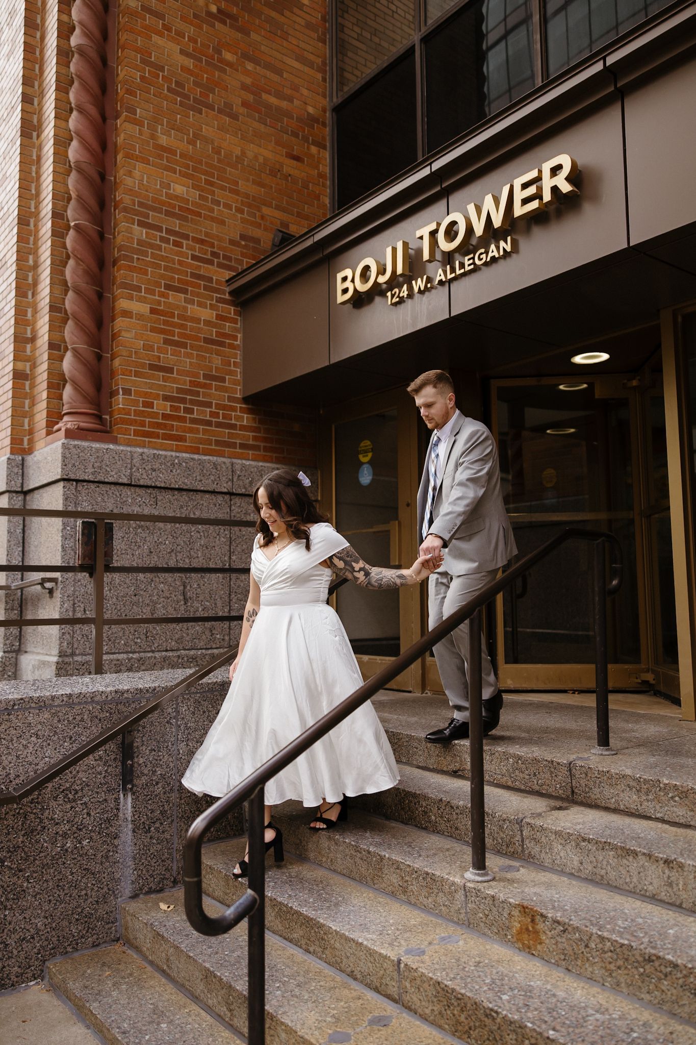 Wedding couple poses playfully on brick building steps with industrial railings.