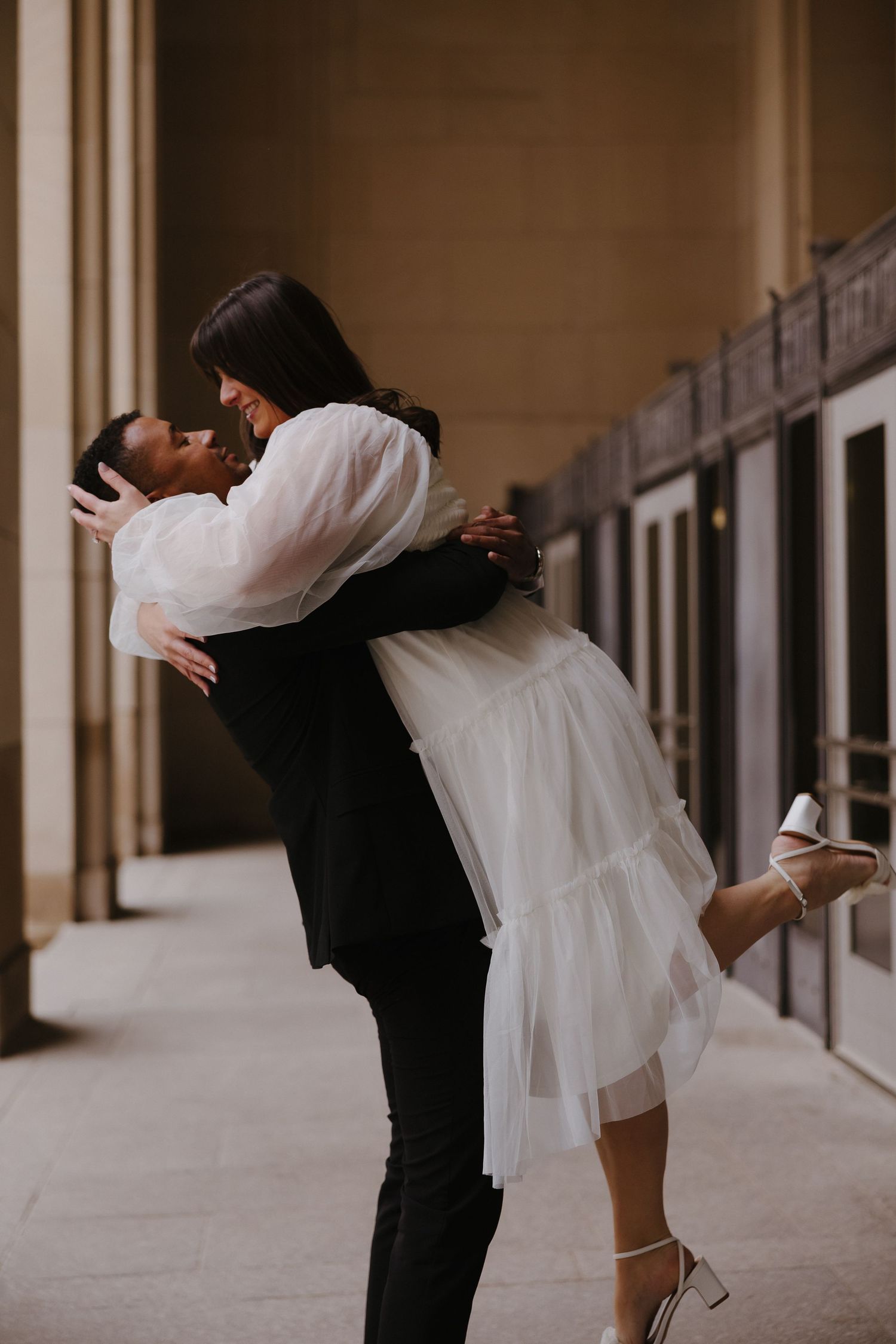 A couple dances and poses playfully in an elegant hallway.
