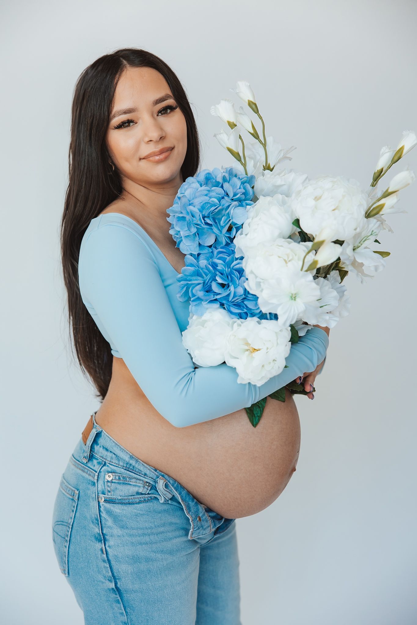 Woman in blue top and jeans holding beautiful blue and white floral arrangement.