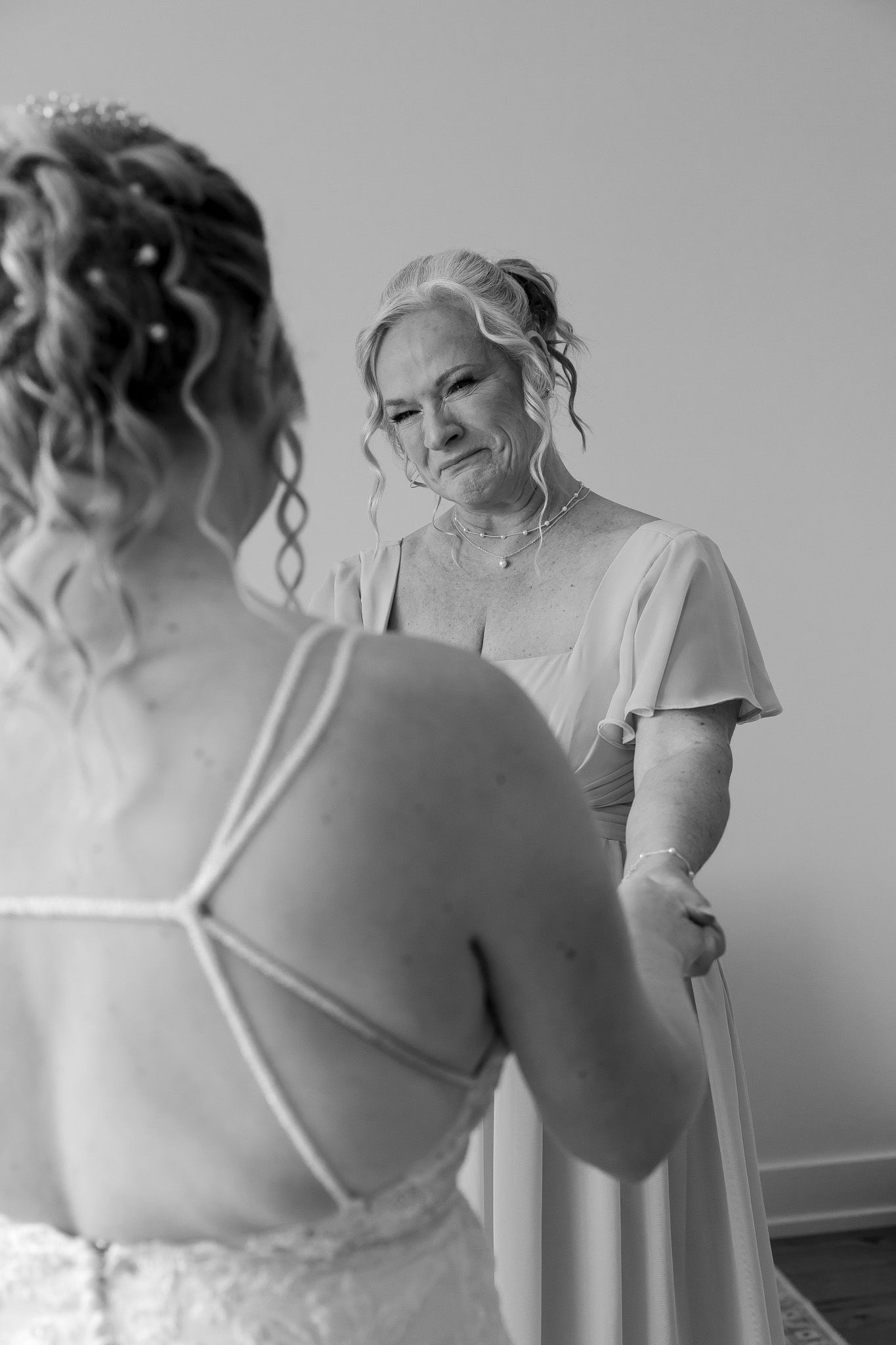 Black and white photo of emotional mother helping bride in wedding dress during bridal preparation.