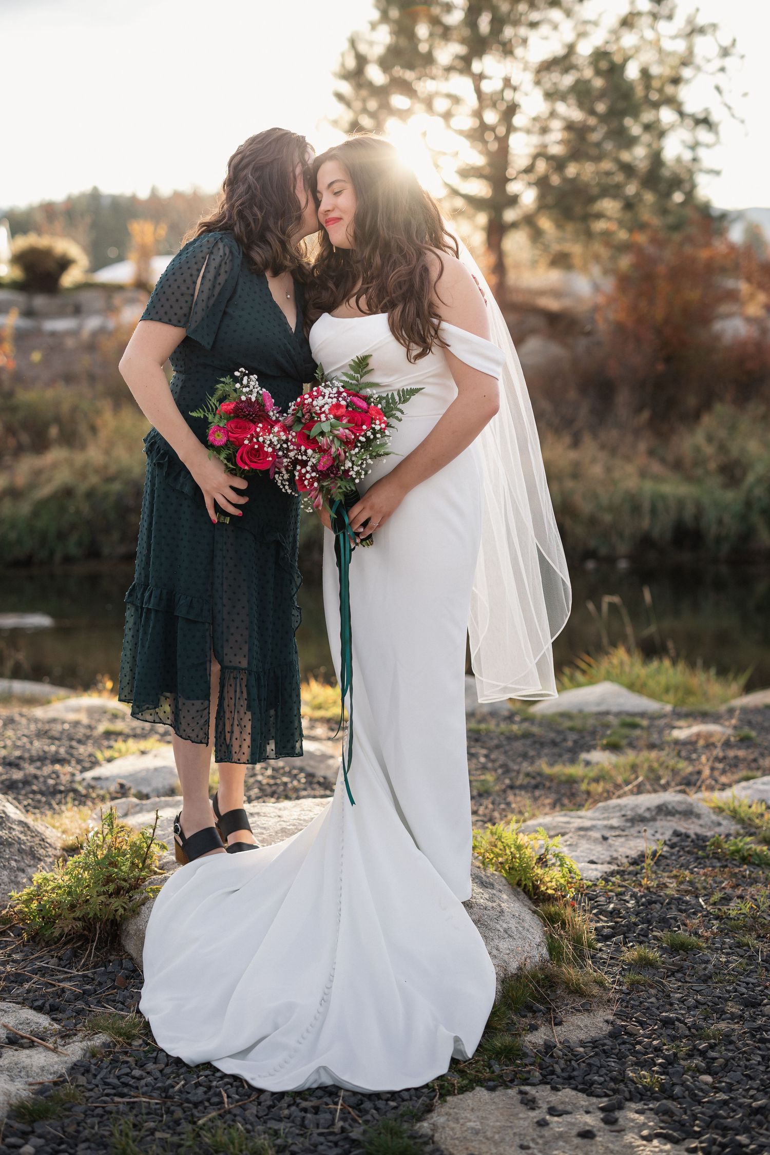 Tender moment between wedding couple in sunlit outdoor setting with flowing white gown.