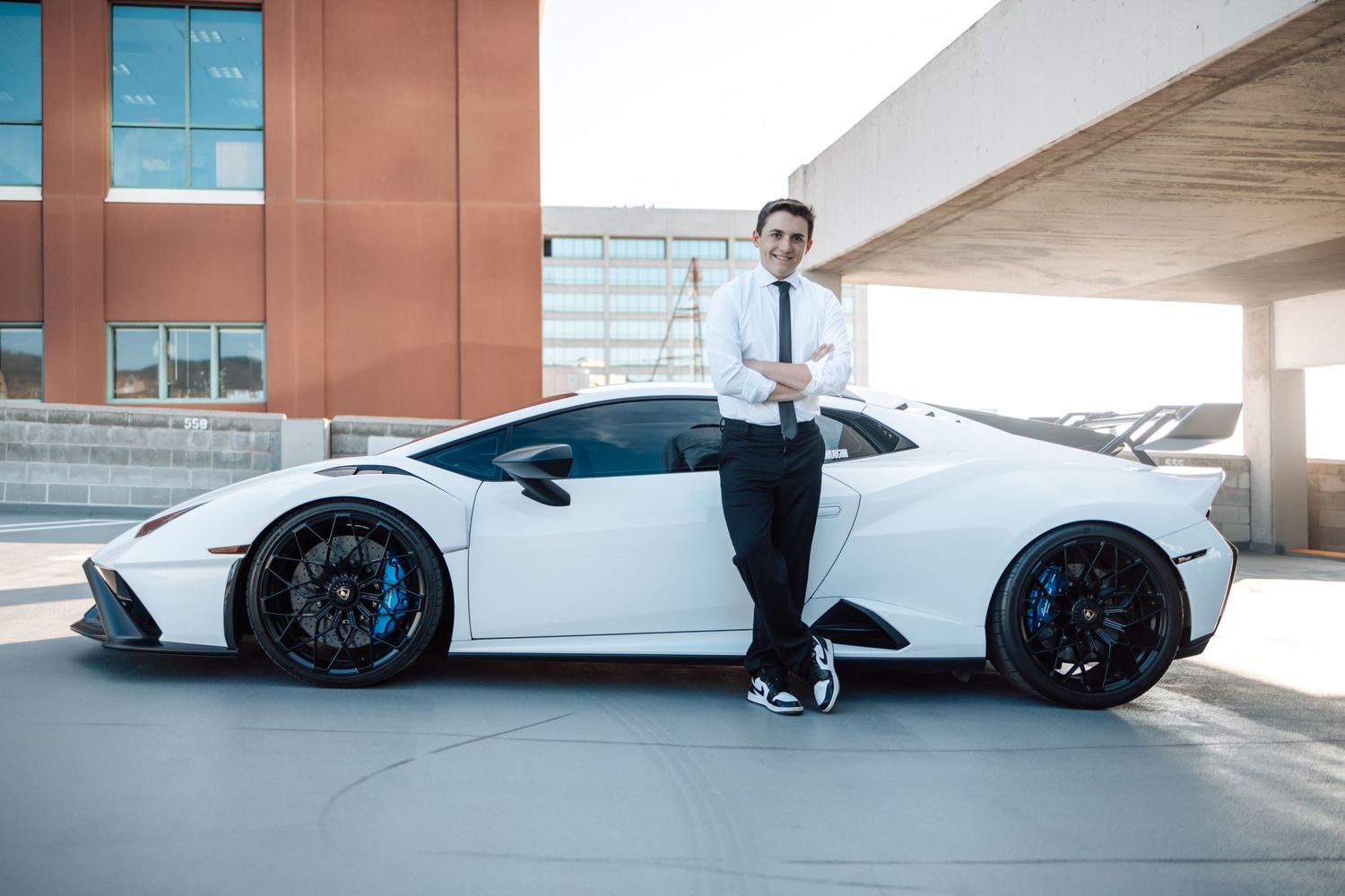 White Lamborghini supercar parked in modern parking structure with person standing beside it.