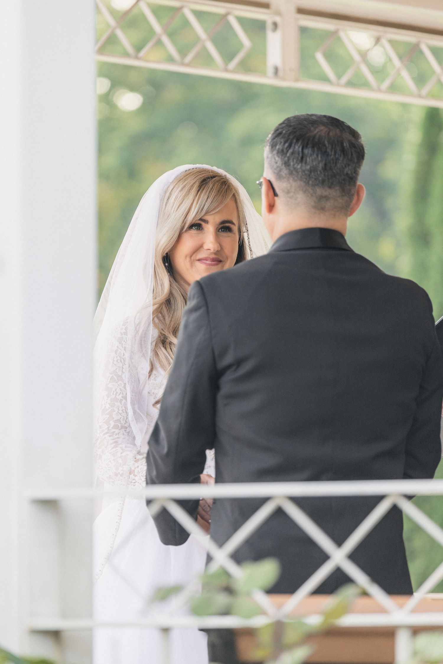 Couple exchanging vows in decorative white gazebo during wedding ceremony.