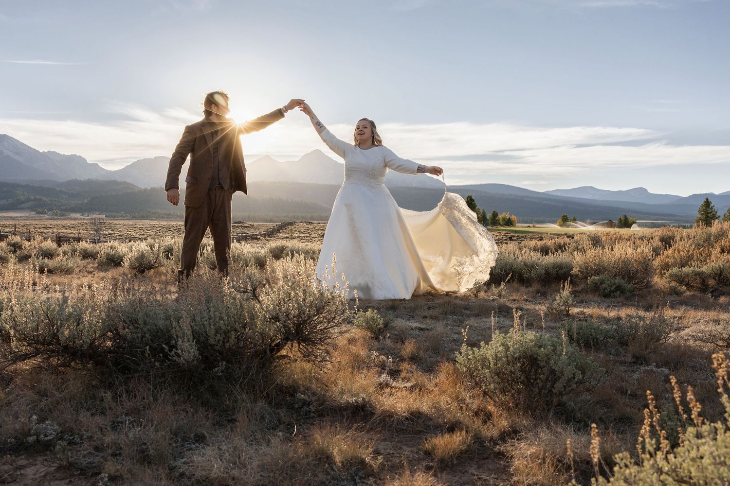 Wedding couple poses in desert landscape with mountains and golden sunlight.
