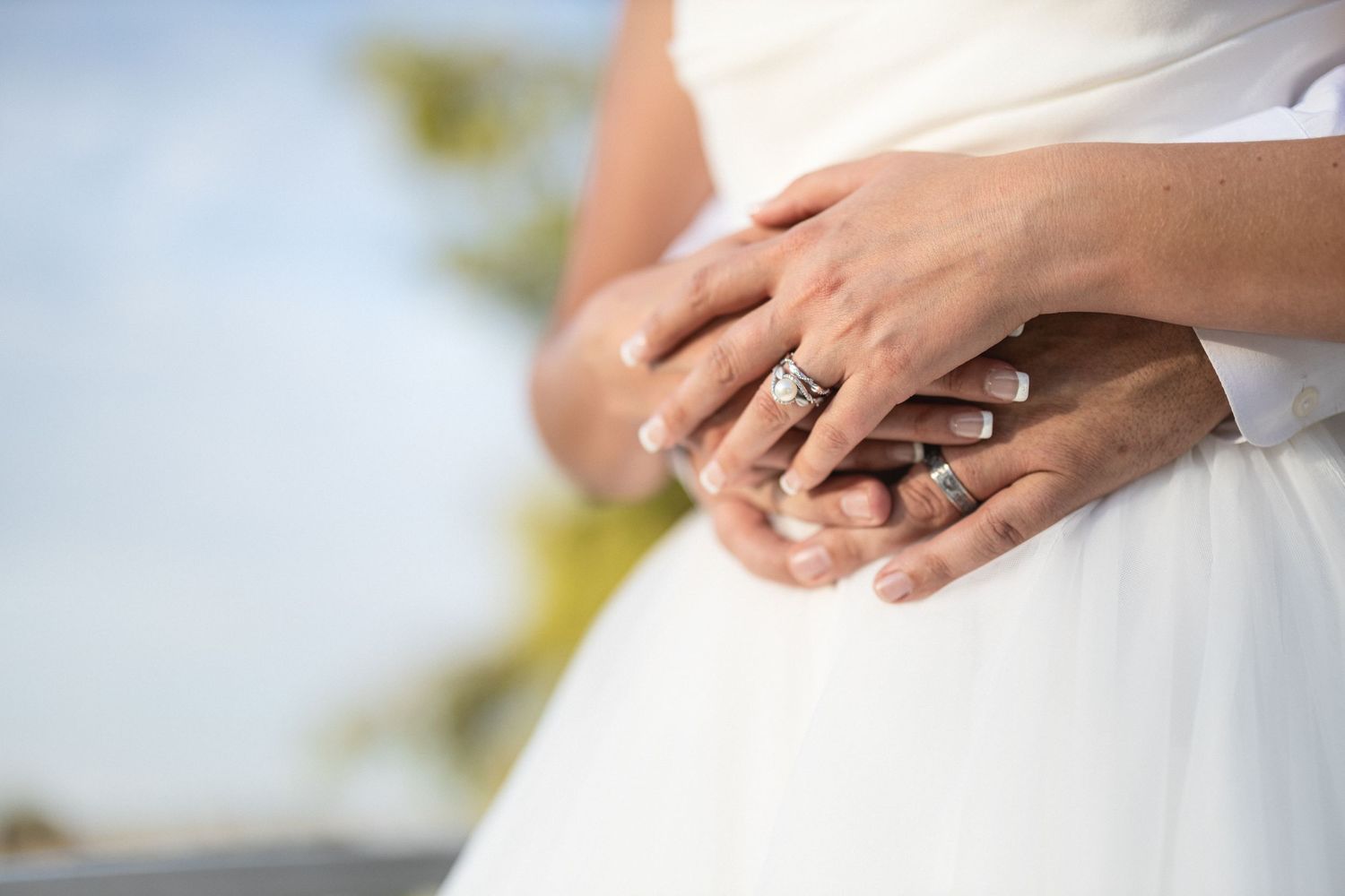 Close-up of hands with wedding rings resting on a white dress.