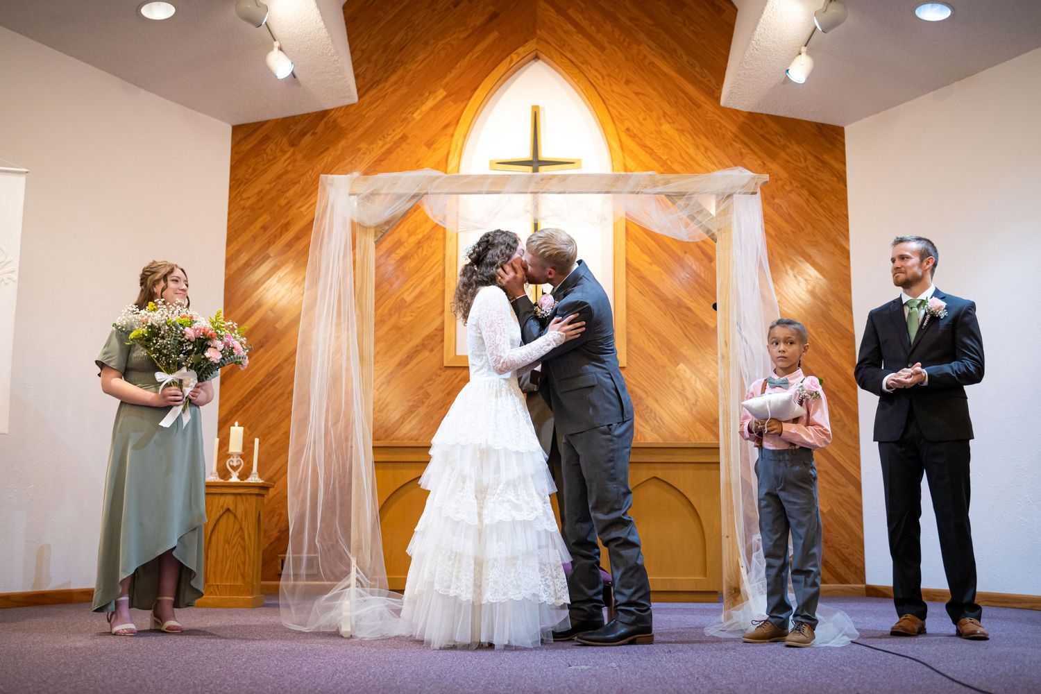 Wedding ceremony moment at church altar with wooden cross backdrop.