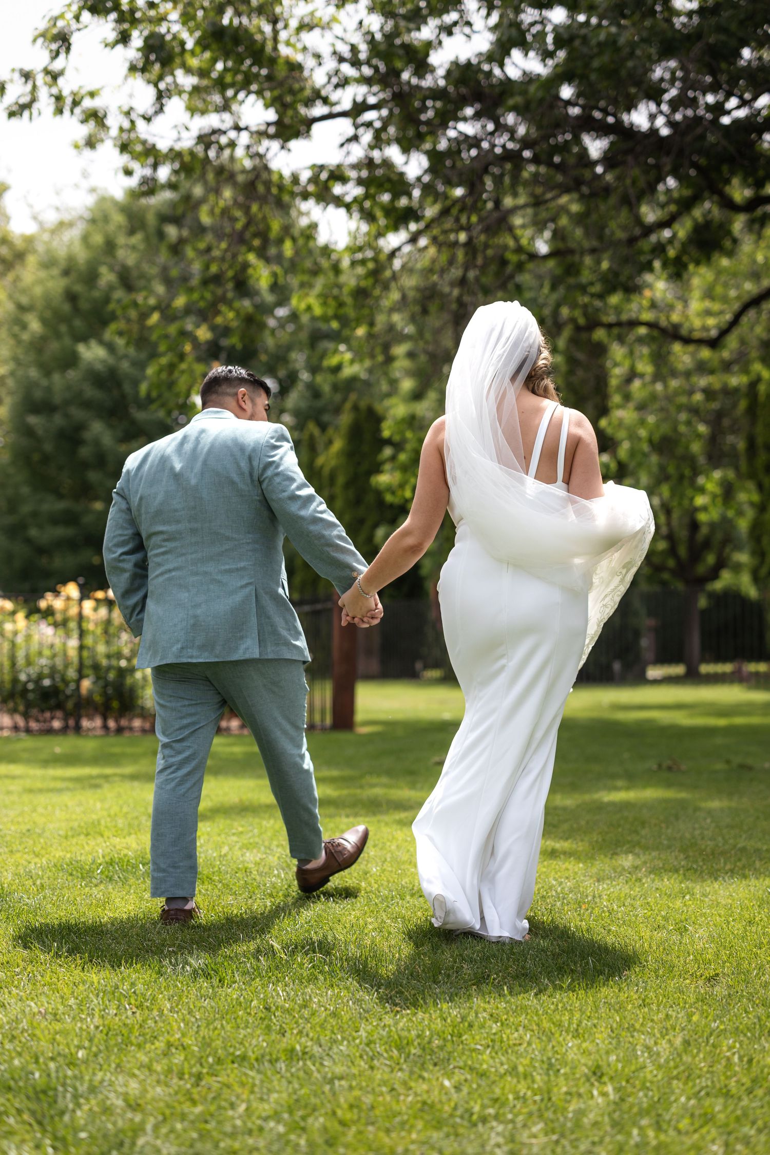 Newlyweds walking hand in hand through lush garden landscape.