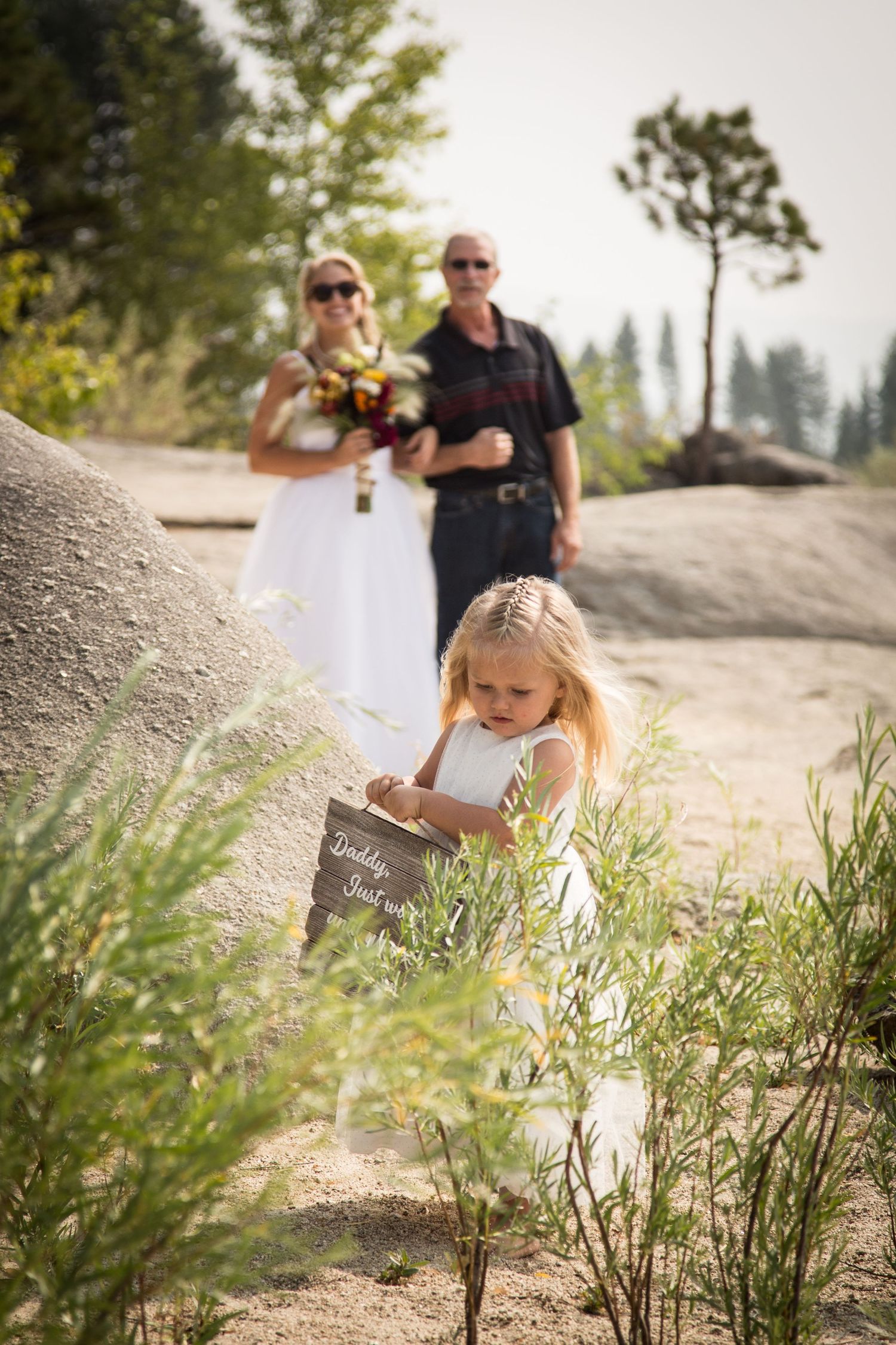 Young flower girl writing on chalkboard during outdoor mountain wedding ceremony.