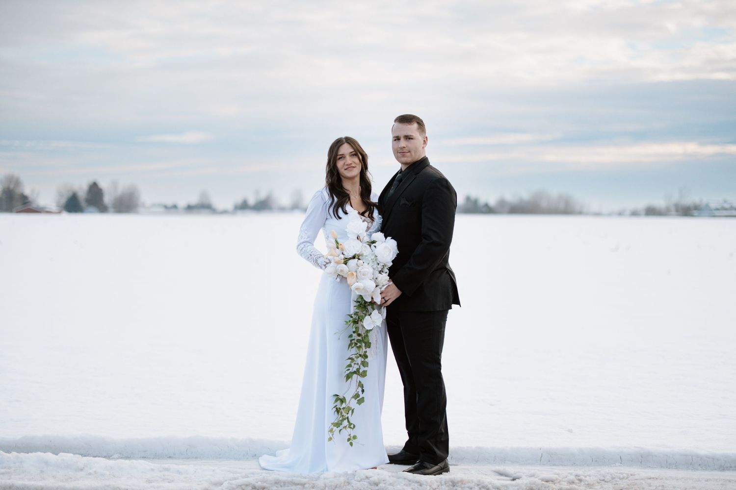 Winter wedding portrait with snowy landscape and flowing cascading bouquet.