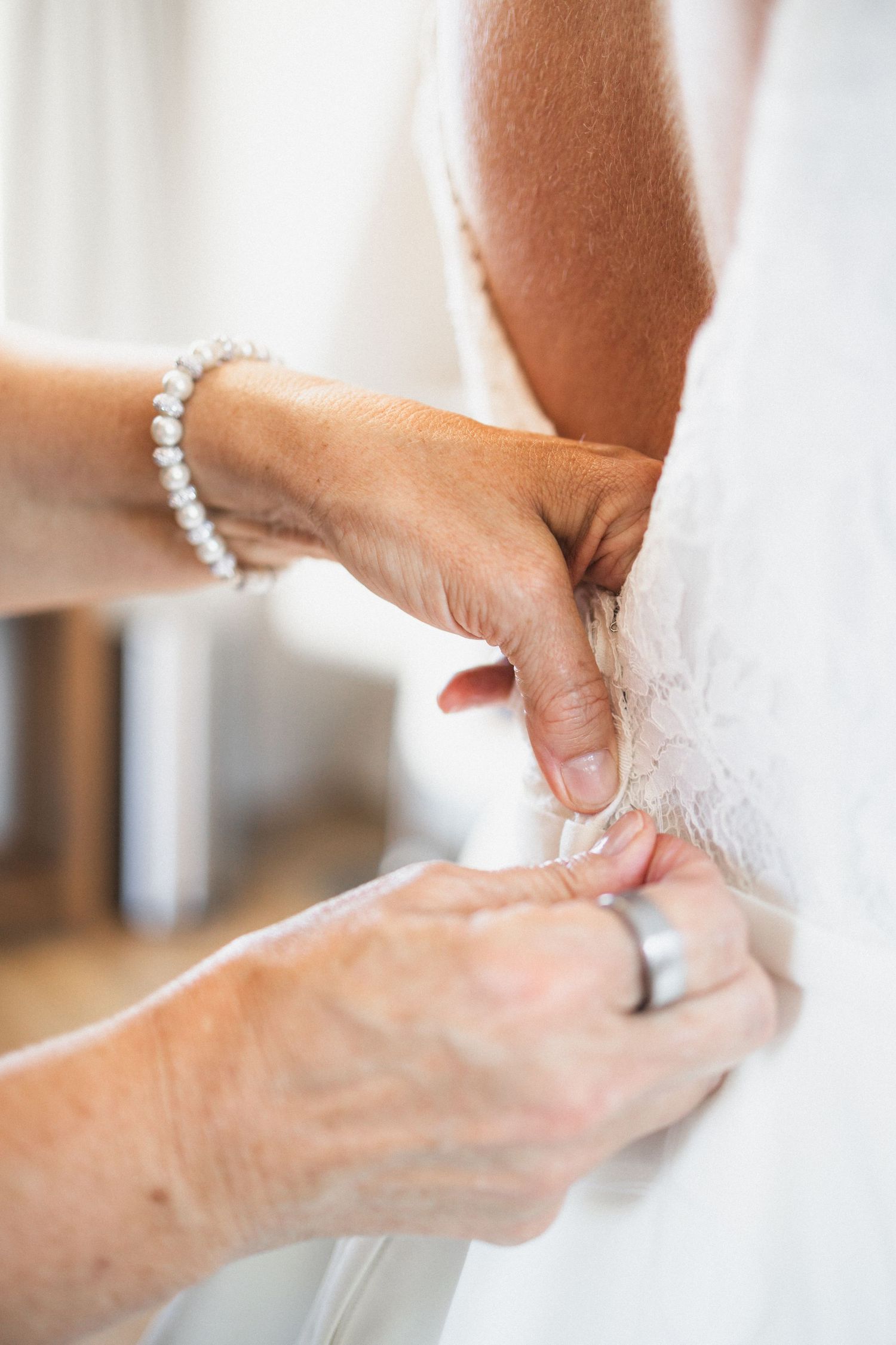 Close-up of hands adjusting a white wedding dress while wearing a pearl bracelet.
