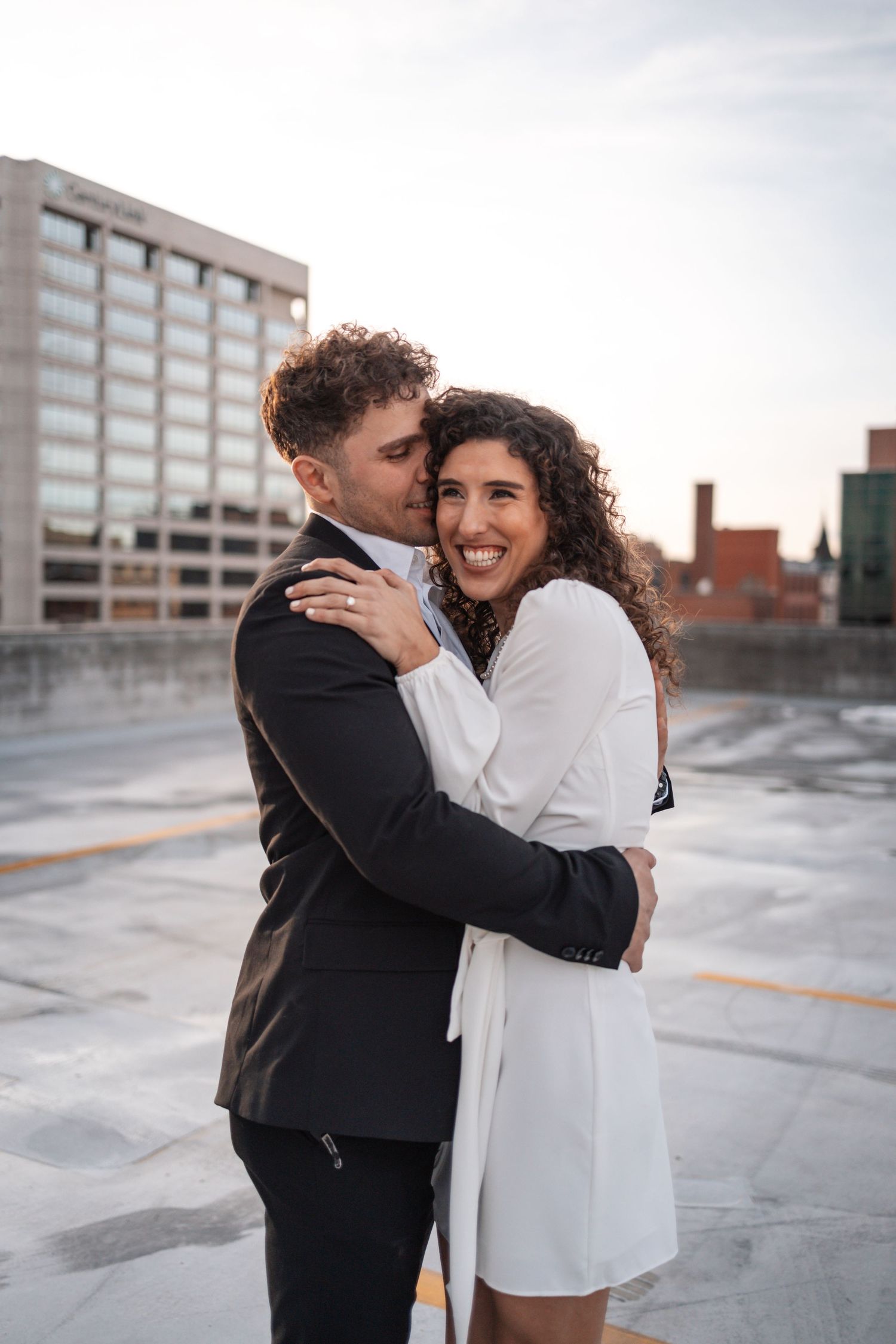 Intimate rooftop moment with couple embracing against urban backdrop.