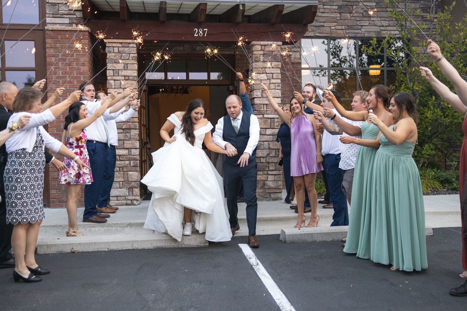 Newlyweds make their grand exit while guests line the pathway outside a stone building.