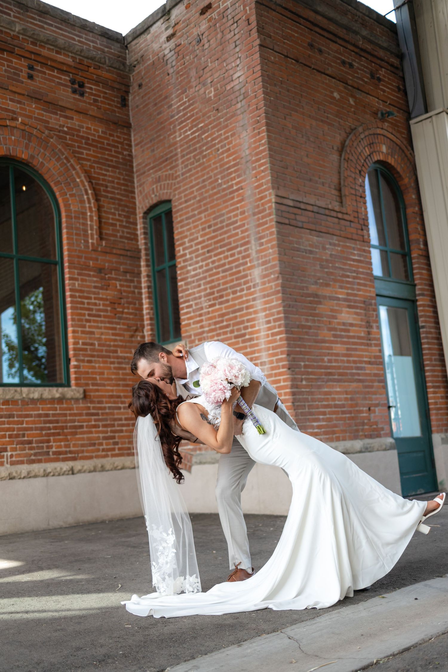 Dramatic dip pose of newlyweds in front of vintage brick building.