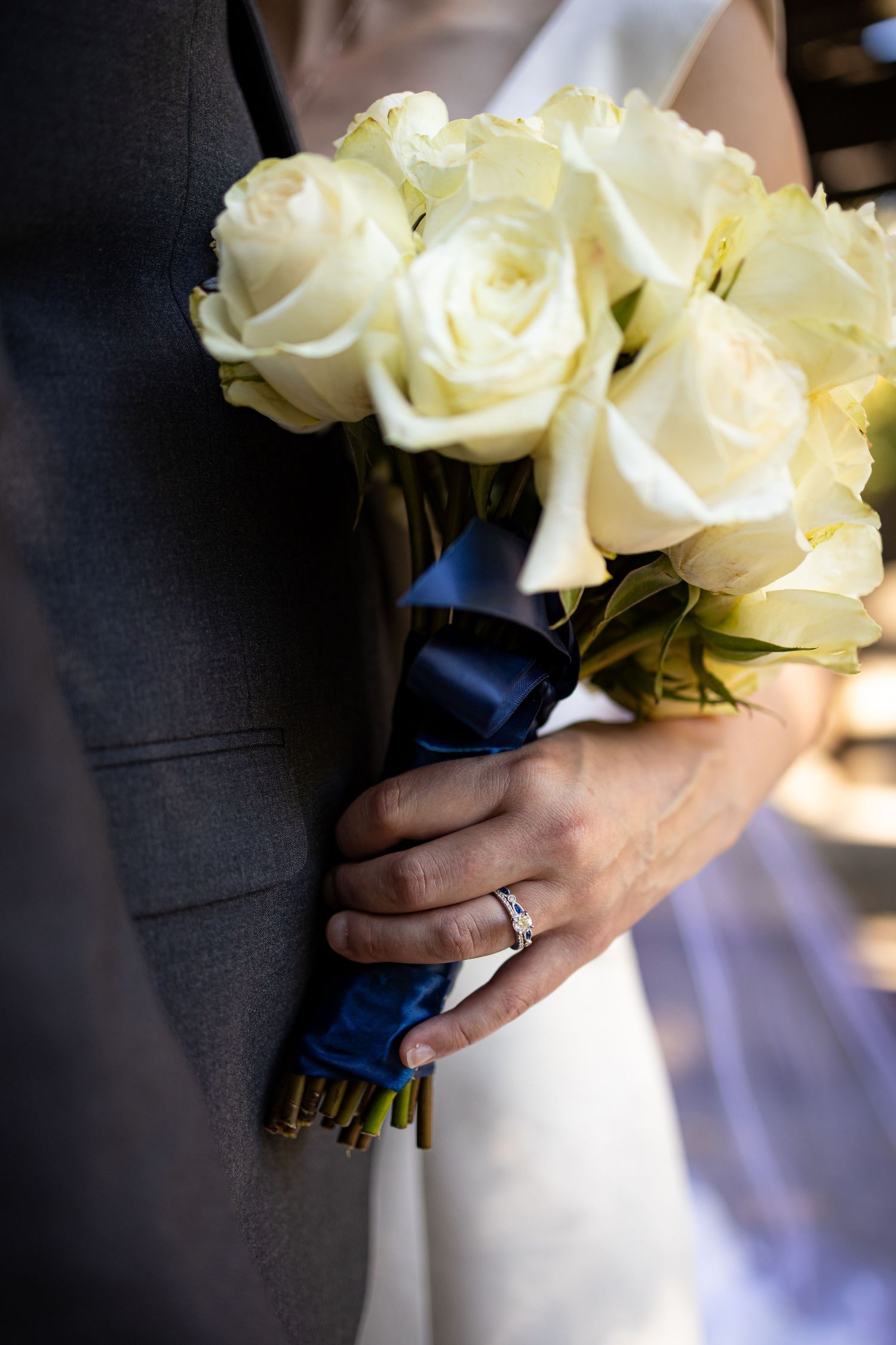 Close up of white rose bridal bouquet with navy ribbon wrap and engagement ring.