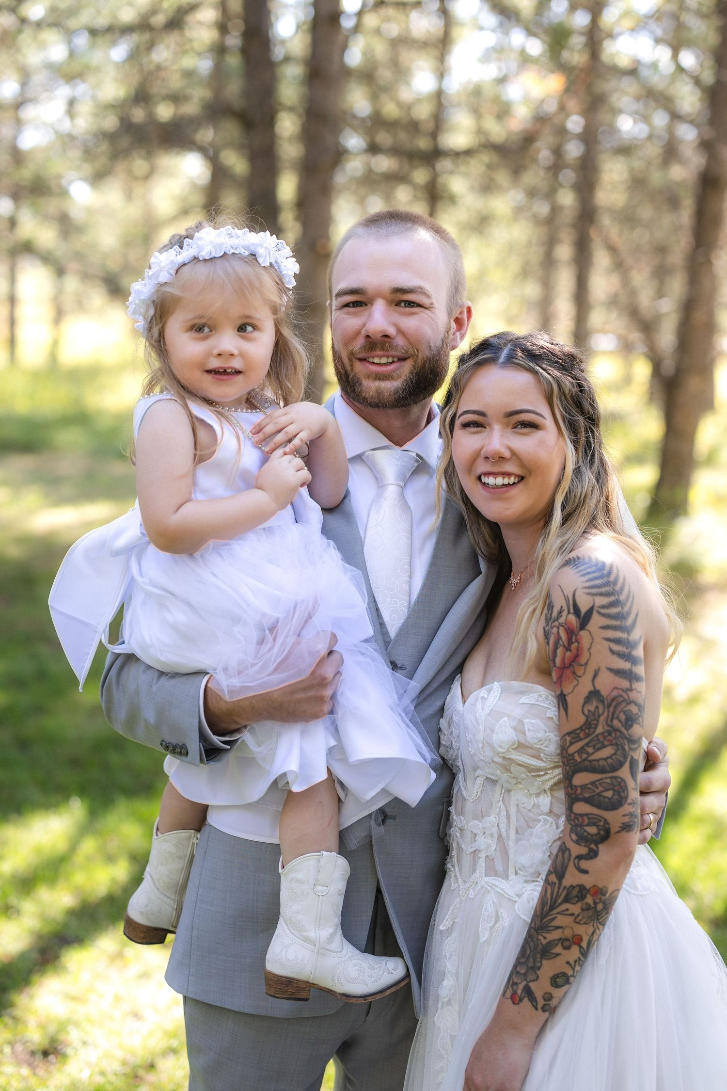 Wedding portrait of a happy family in formal attire standing in a sunlit forest.