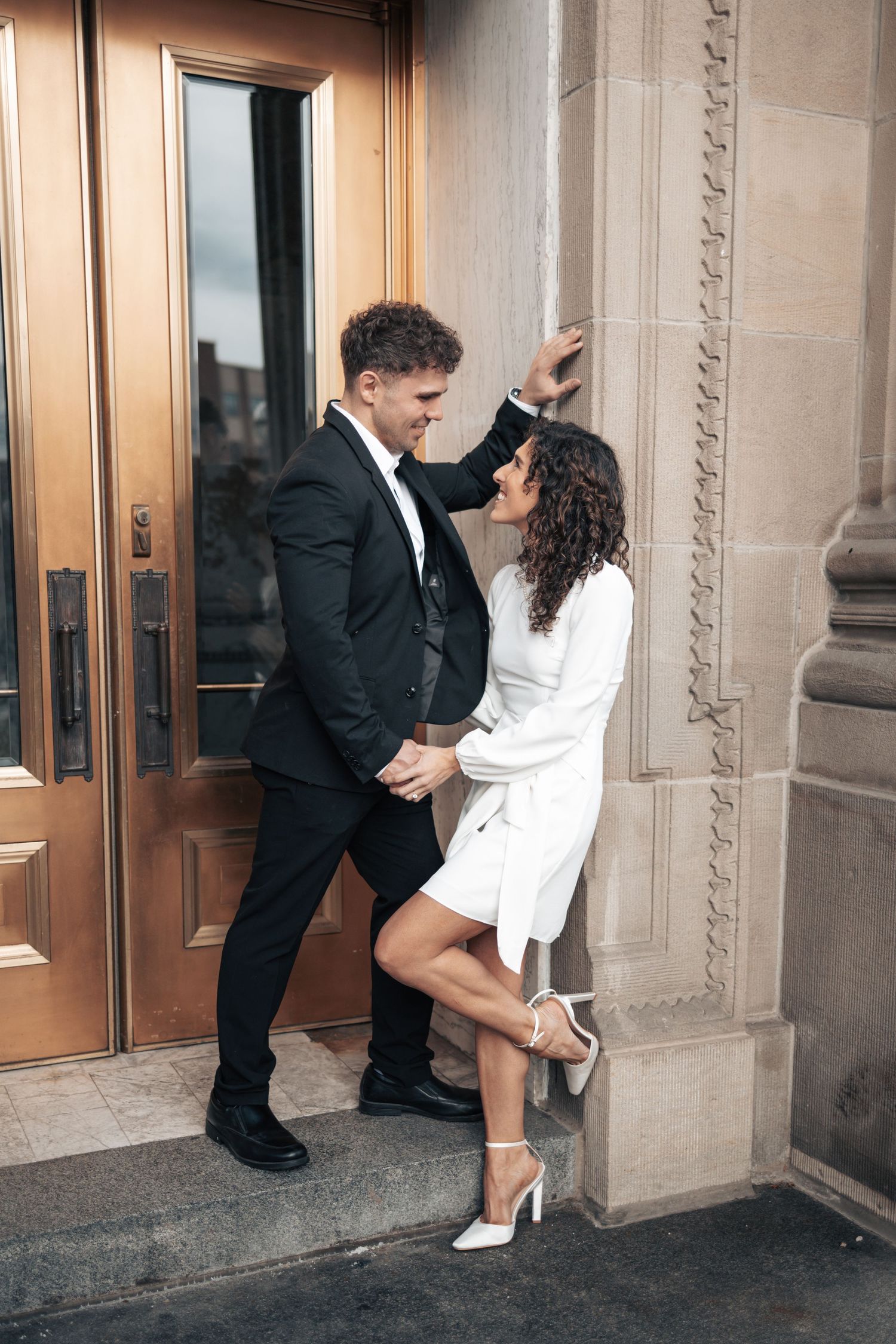 Romantic couple poses against building exterior in contrasting black and white formal wear.